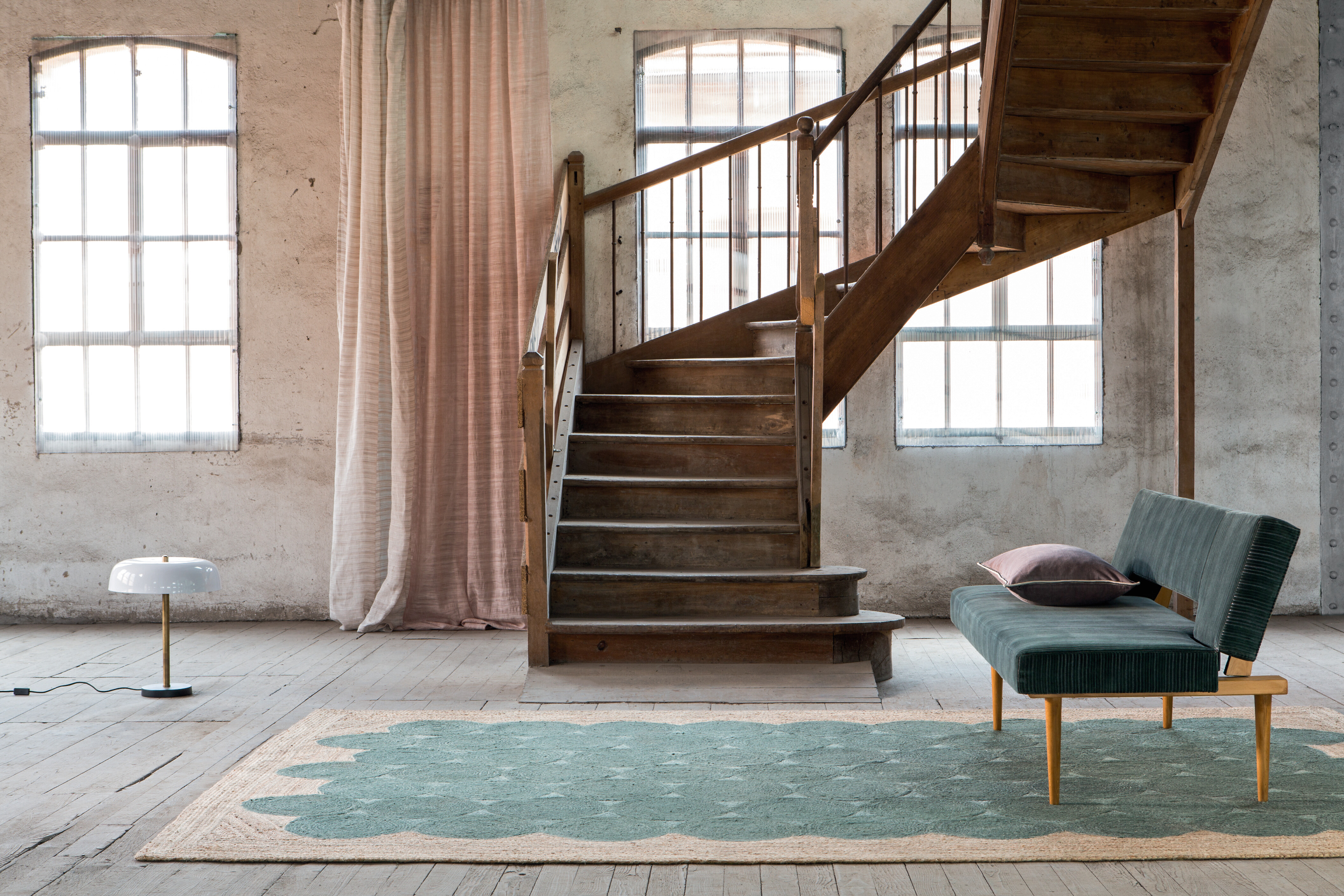 Holztreppe in hellem Raum mit grünem Teppich und Vorhang in zartem Rosa vor gealterten Wänden
