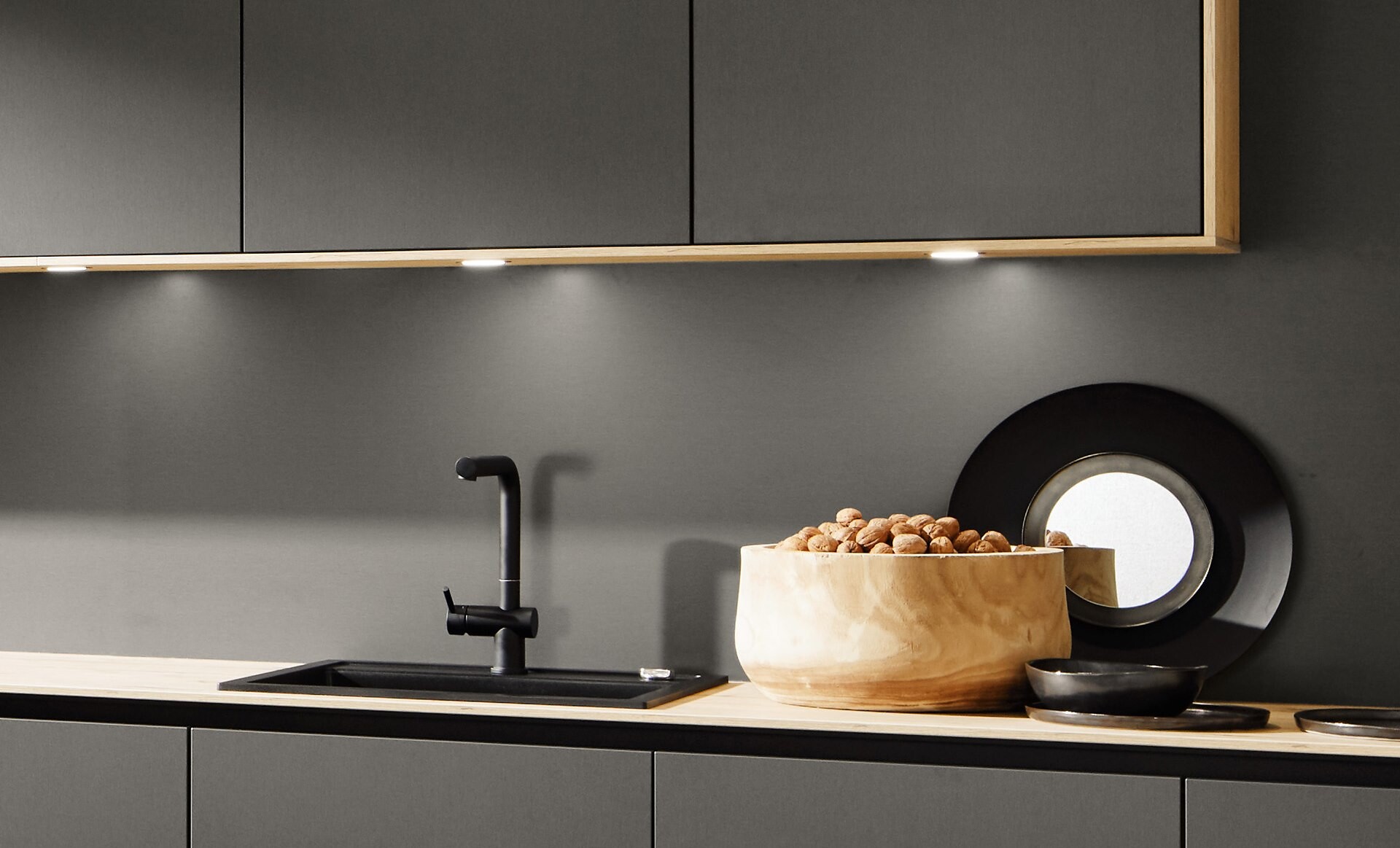 Graue Nolte Küchenzeile mit schwarzen Armaturen und stimmiger Beleuchtung