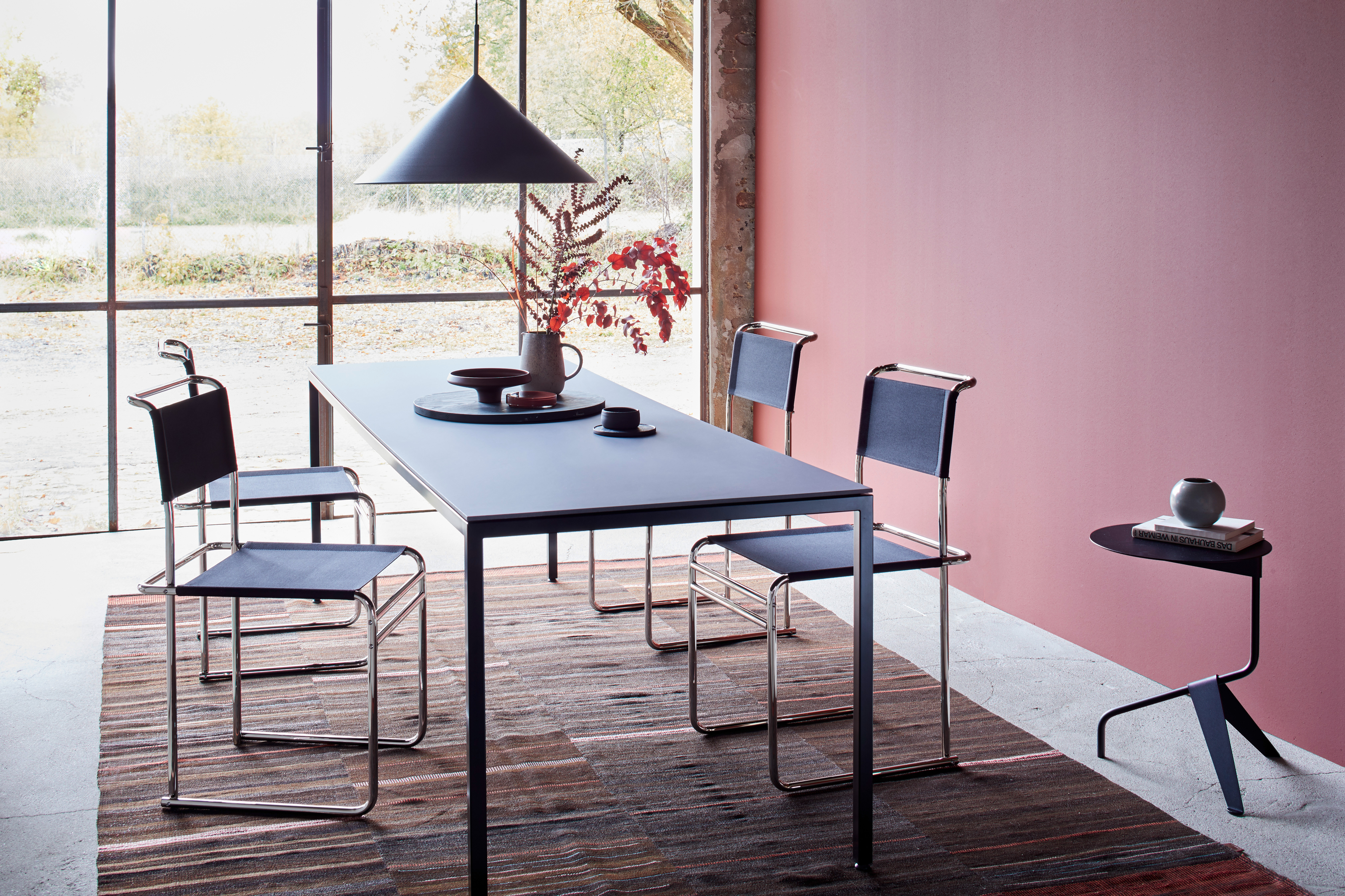 schwarze Stahlrohrstühle an schwarzem Esstisch vor rötlicher Wand
