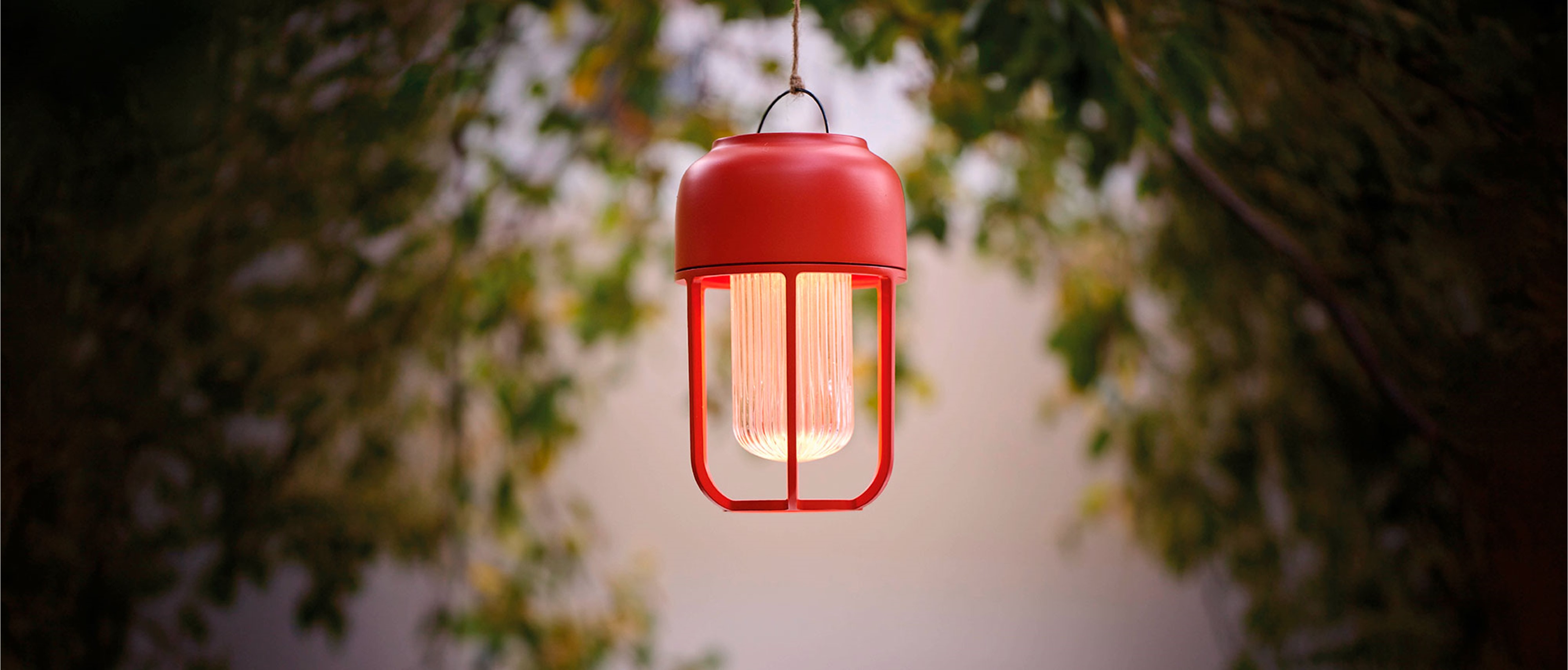 Solarleuchte Light No1 von Houe in Rot, aufgehängt vor verschwommenem Hintergrund mit Blättern.