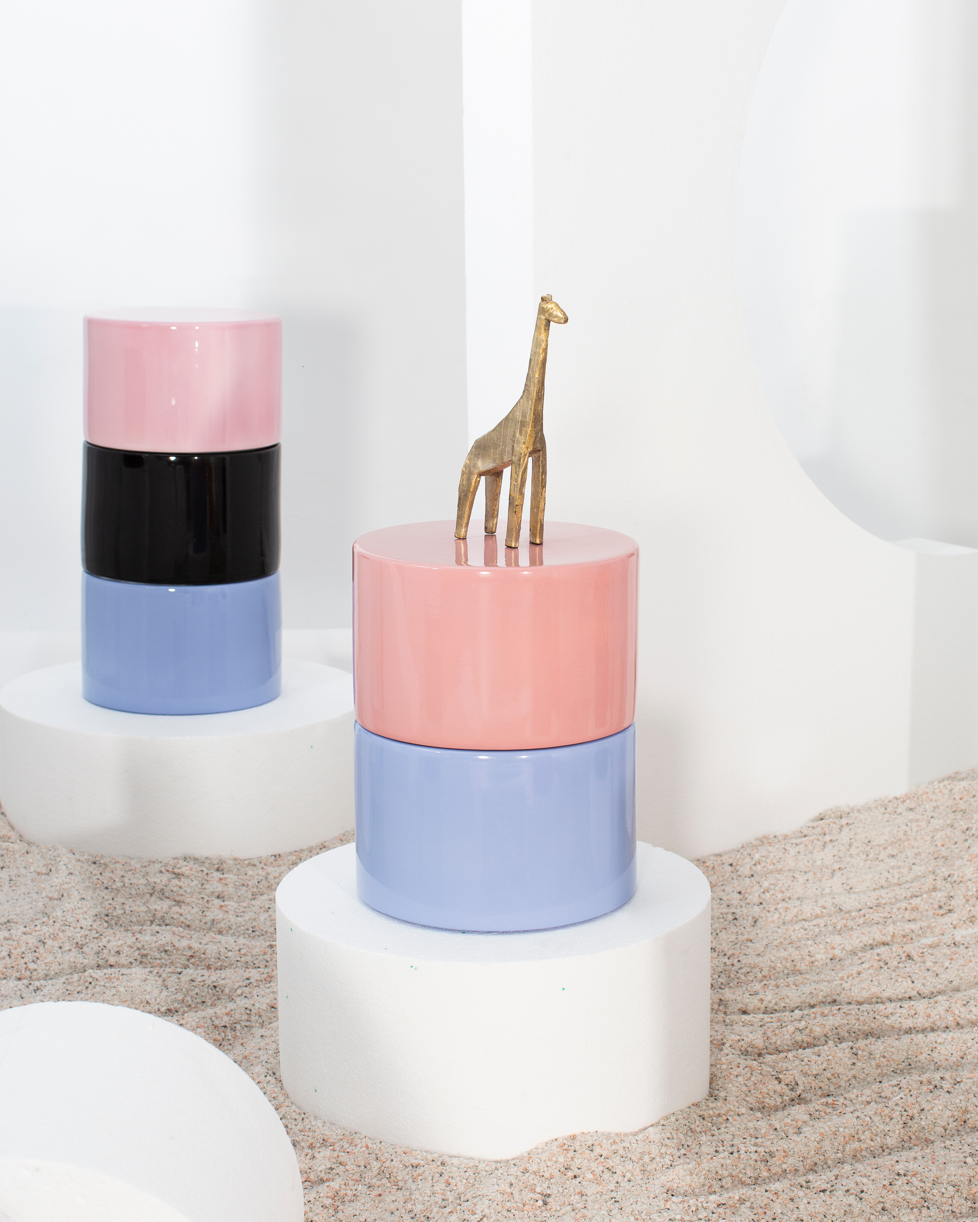 Zylindrische Beistelltische in Pastellfarben mit Dekofigur auf weißem Podest