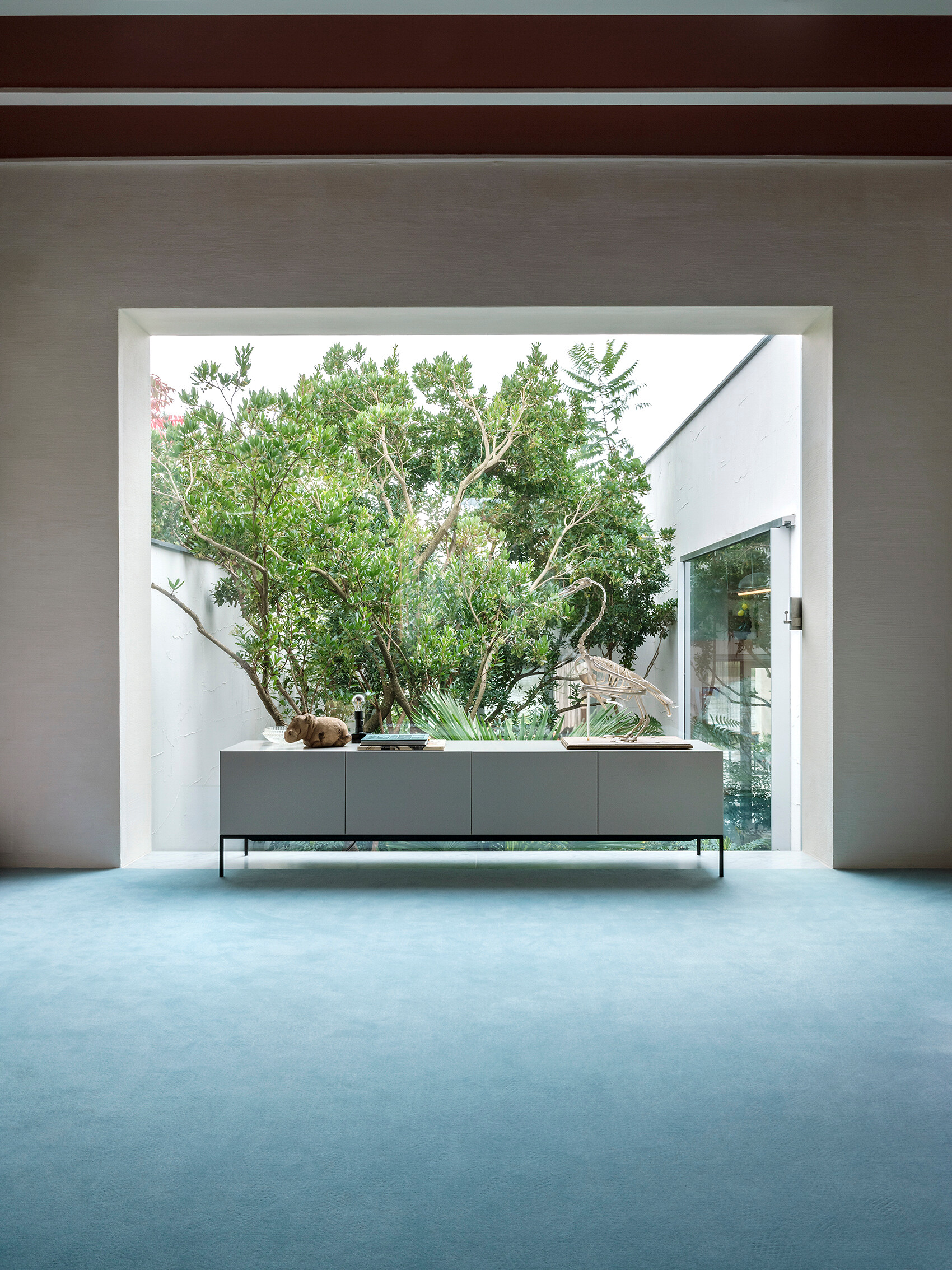 Schlichtes Sideboard vor raumhohem Fenster mit Blick ins Grüne in einem lichtdurchfluteten Interieur