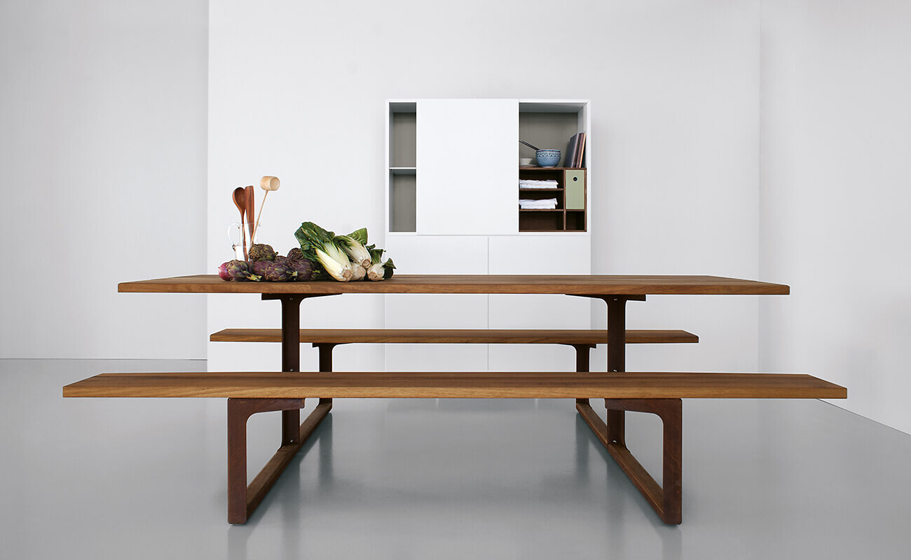 Puristischer Esstisch mit zwei integrierten Bänken aus Holz vor weißer Wand und Stauraumregal