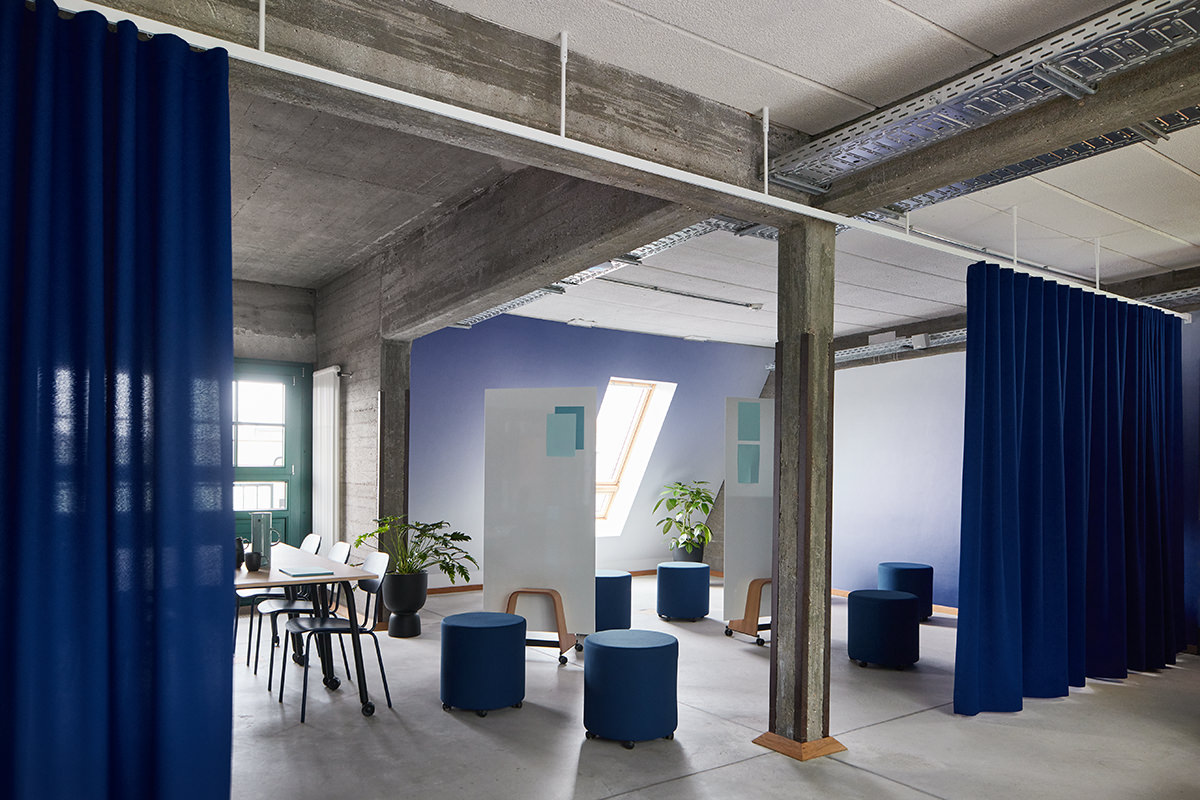 SPACE nextMedia: modernes "New Work"-Konzept. Flexible Arbeitsbereiche mit blauen Vorhängen, mobilen weißen Trennwänden und ergonomischen blauen Sitzpoufs, immer neu konfigurierbar.