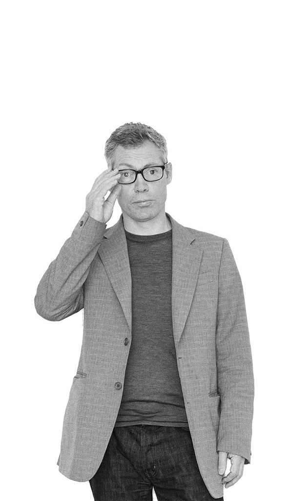 Jasper Morrison im Porträt, stehend in legerem Sakko, mit Brille und ruhigem Blick, vor weißem Hintergrund.