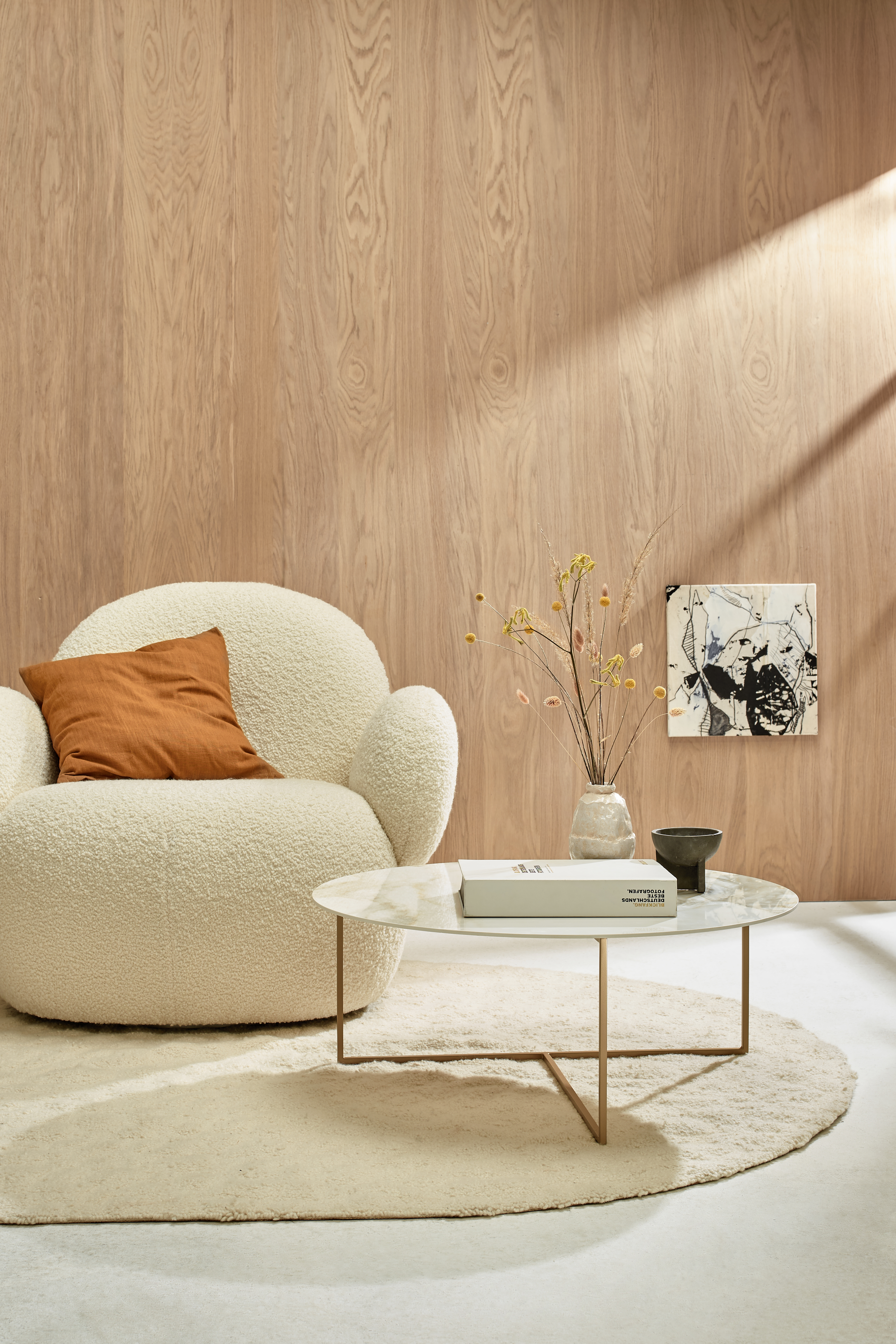 Runder Sessel in Wolloptik mit Beistelltisch auf hellem Teppich vor Holzvertäfelung  