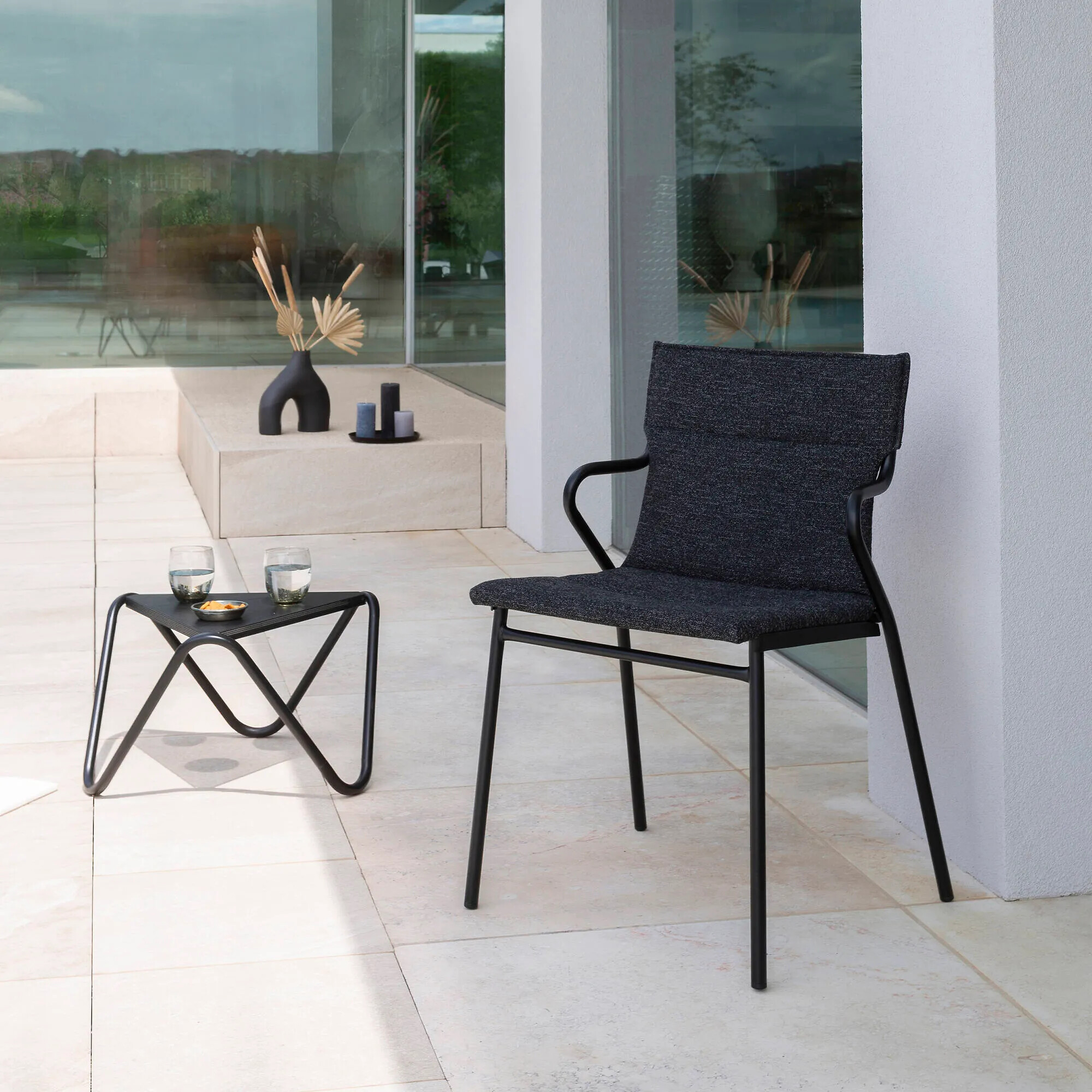 Schwarzer Outdoor-Stuhl mit passendem Beistelltisch aus Metall auf heller Terrasse