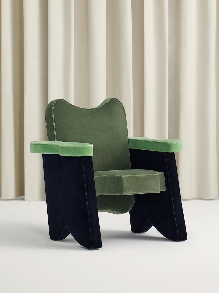 Sessel mit grüner Polsterung und markant geschwungener Form vor Vorhang