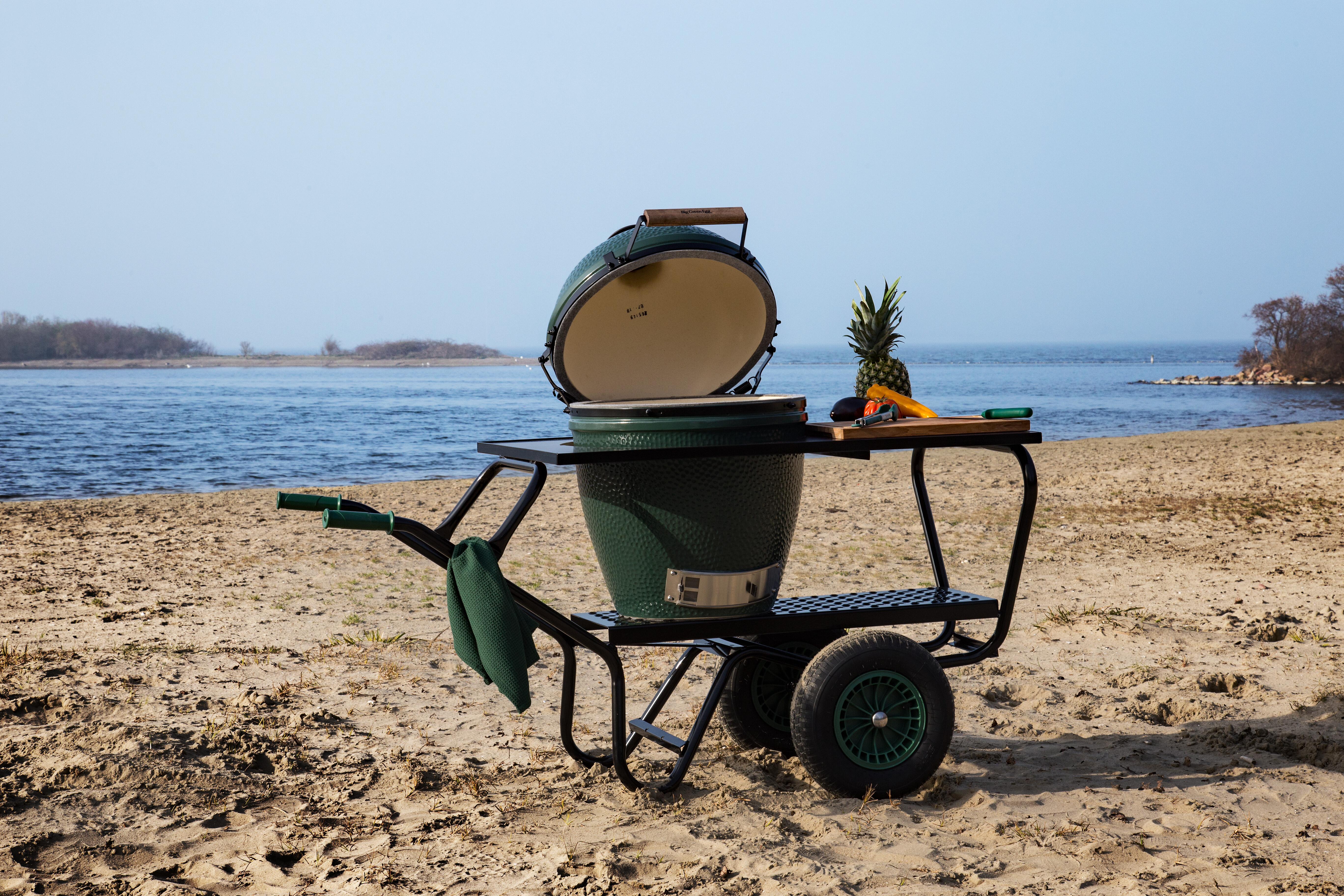 Mobiler Big Green Egg Grill auf rollbarem EGGmover mit Zubehör am Sandstrand platziert  