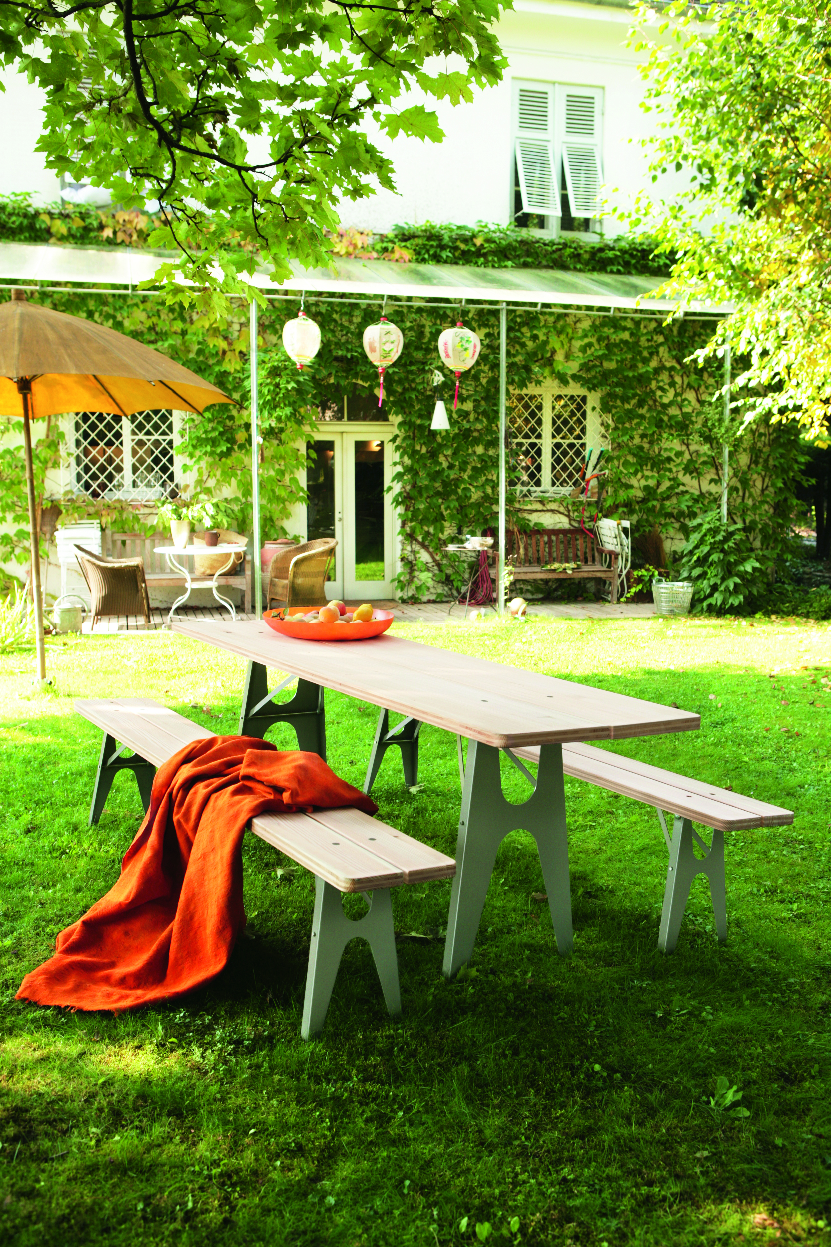 Gartenbank-Set mit orangefarbener Decke vor grün bewachsener Hausfassade