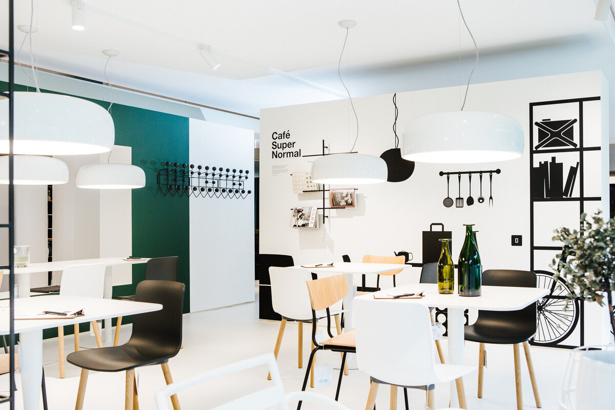 Café Supernormal mit weißen und schwarzen Stühlen, minimalistischer Einrichtung und Wandgrafik.