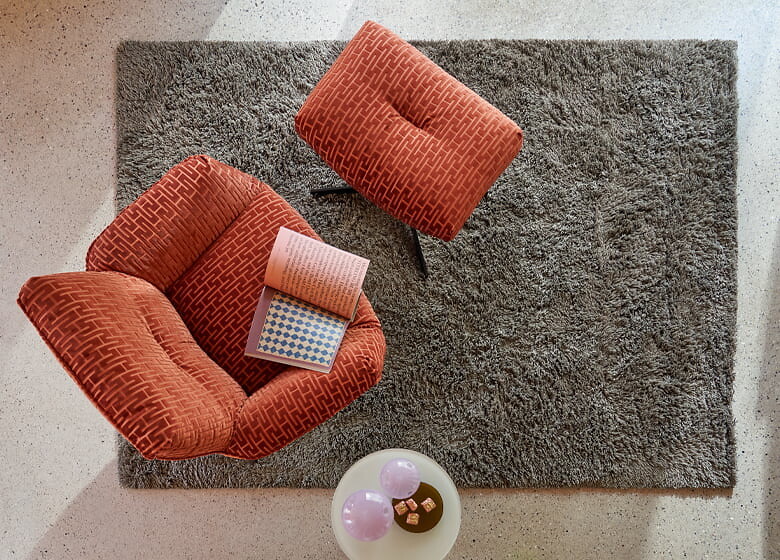 Hochflorteppich in Grau unter rotem Polstersessel mit passendem Hocker von oben