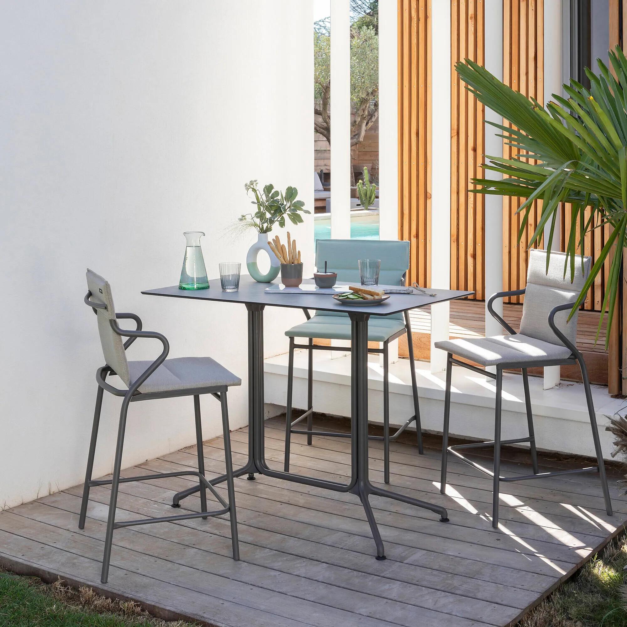 Barhocker Sitzgruppe mit drei Outdoorstühlen und rechteckigem Tisch auf Holzpodest