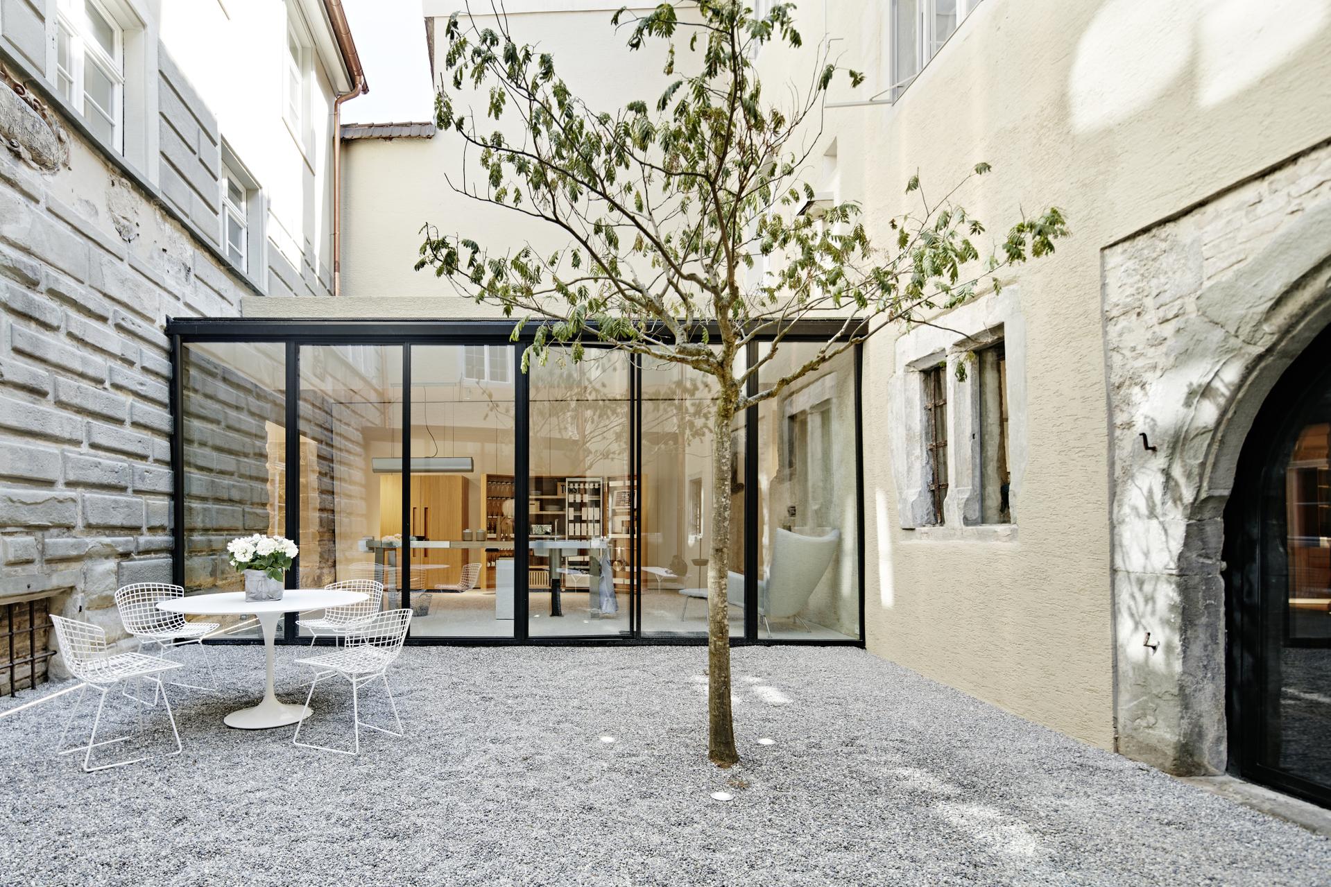 Innenhof von Bulthaup am See mit Sitzgruppe, Kiesfläche und Glasfassade zum Showroom