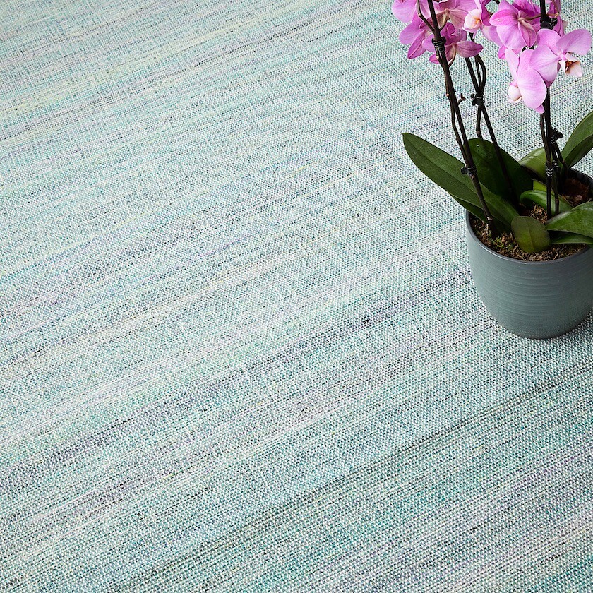 Fein strukturierter Teppich in Aquatönen mit Orchidee in grauem Topf