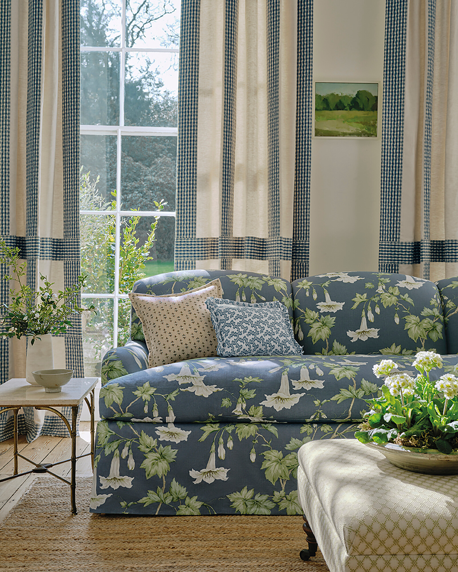 Blaues Sofa mit großflächigem Blütendessin vor bodenlangen Vorhängen  