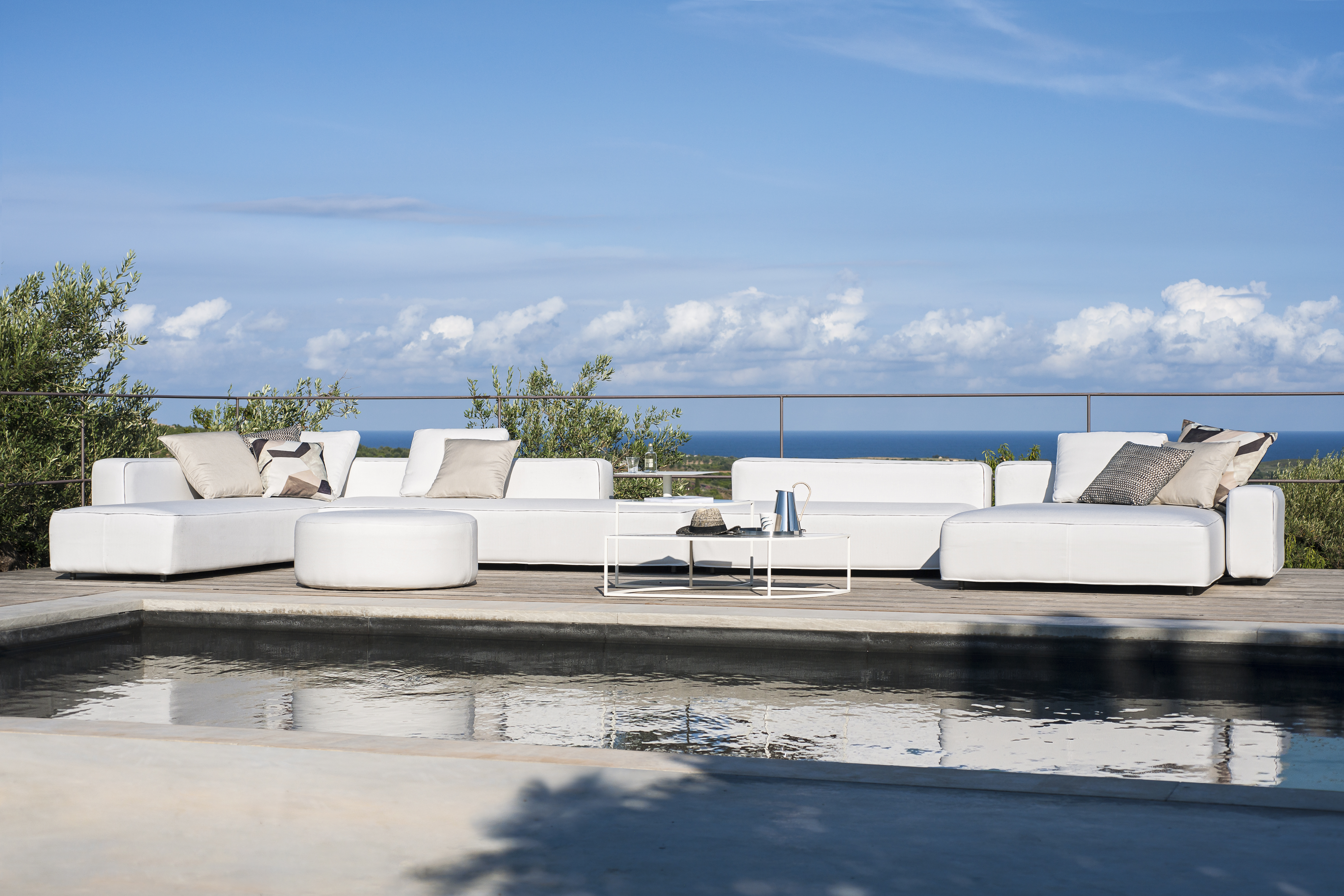 Modulares Outdoor-Sofa in Weiß mit Kissen auf Holzdeck und Meerblick im Hintergrund