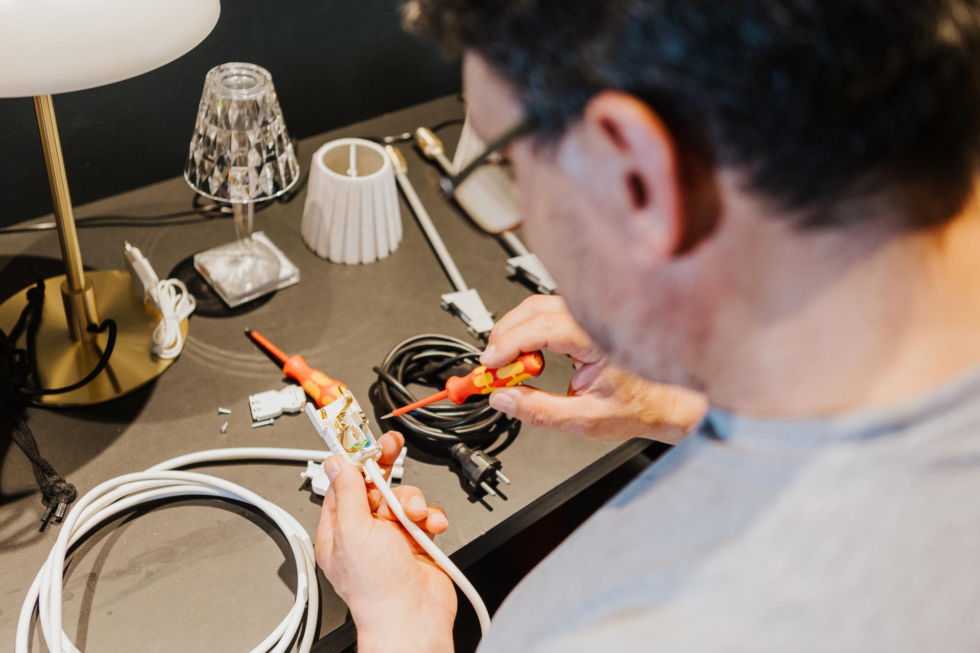 Ein Elektriker von Seipp Wohnen bei der Vorbereitung einer Leuchtenverkabelung an einem schwarzen Arbeitstisch.