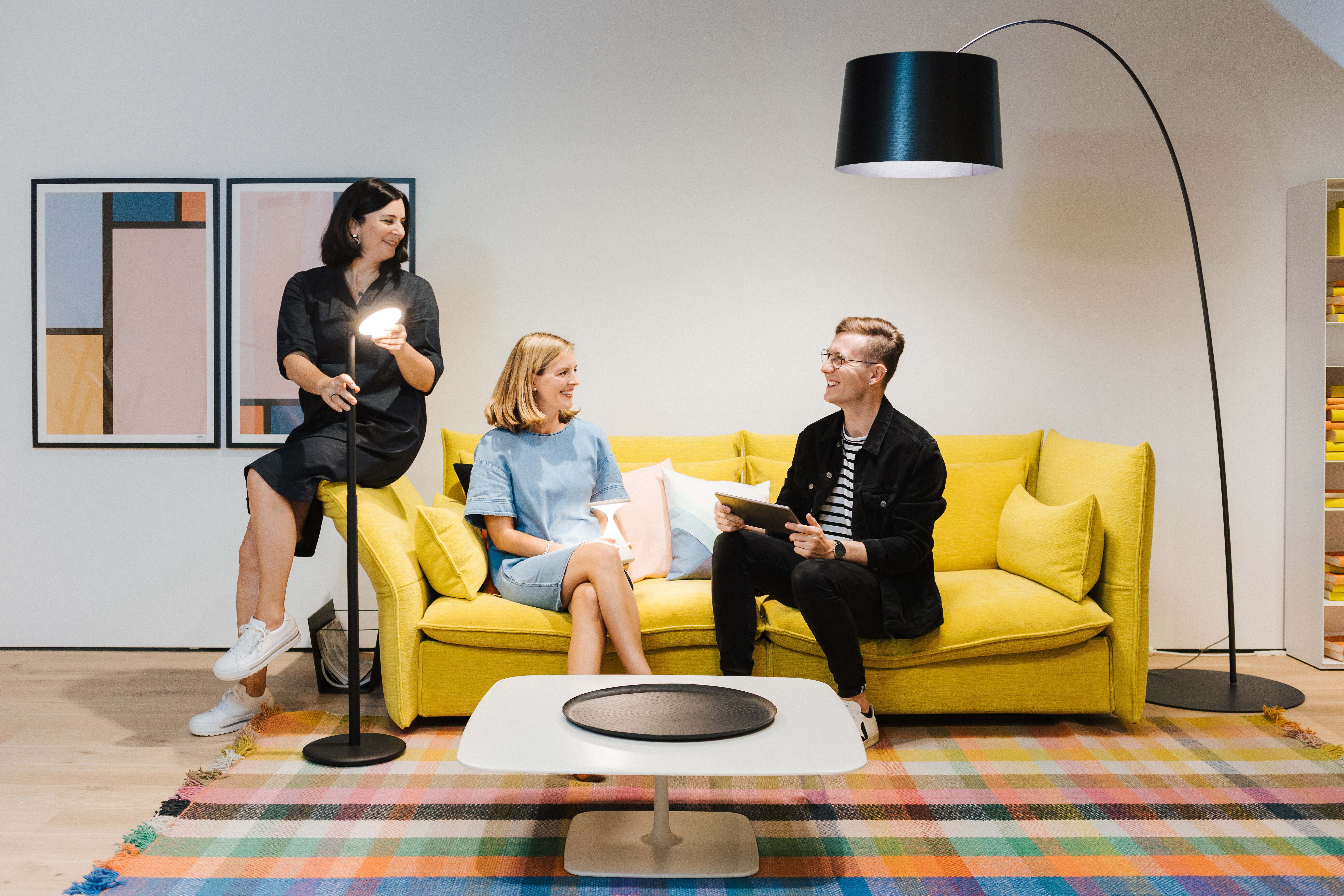 Fachberater der Leuchtenabteilung auf gelbem Sofa mit Stehleuchten und buntem Teppich  