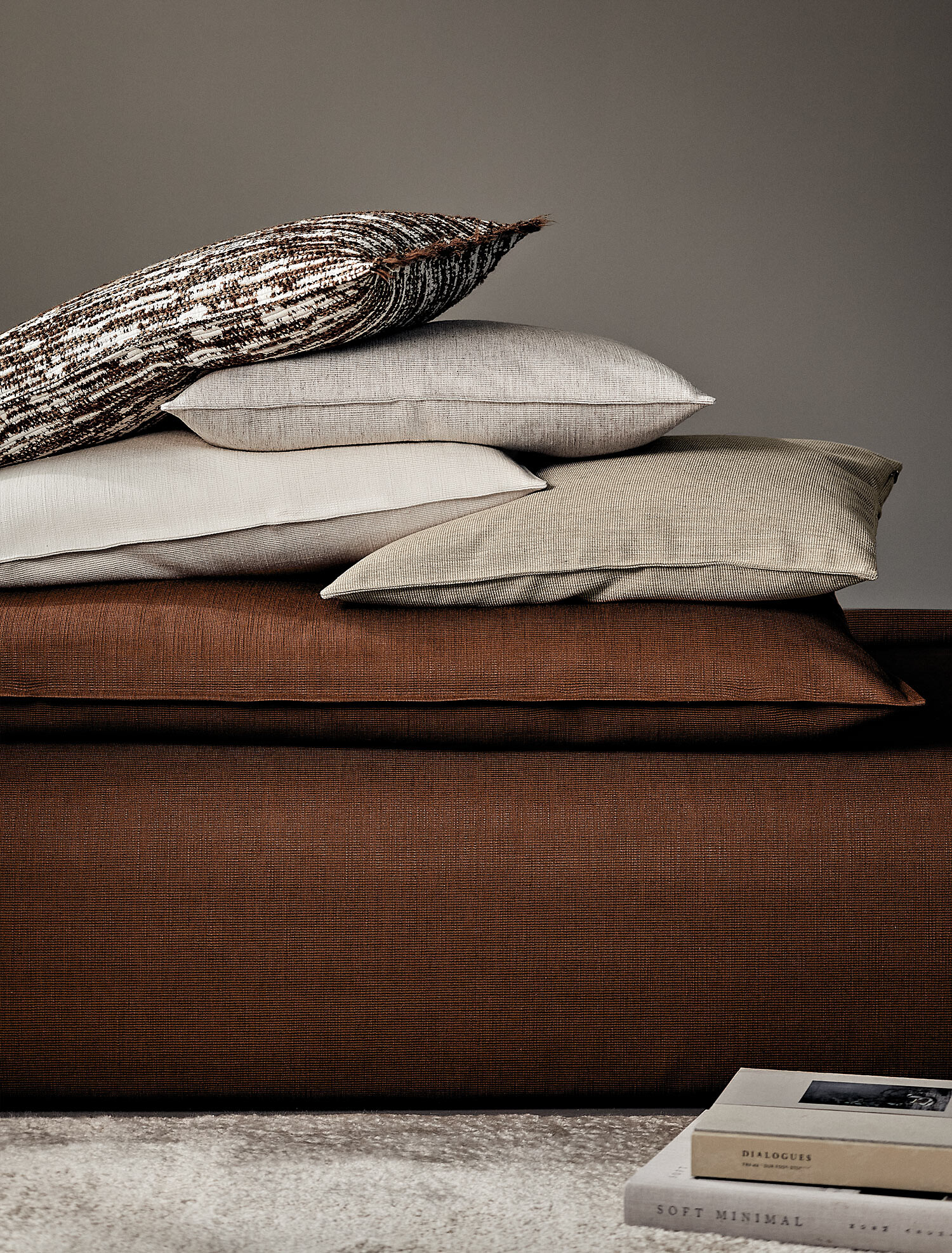 Stapel weicher Kissen in Erd- und Naturtönen vor neutralem Hintergrund