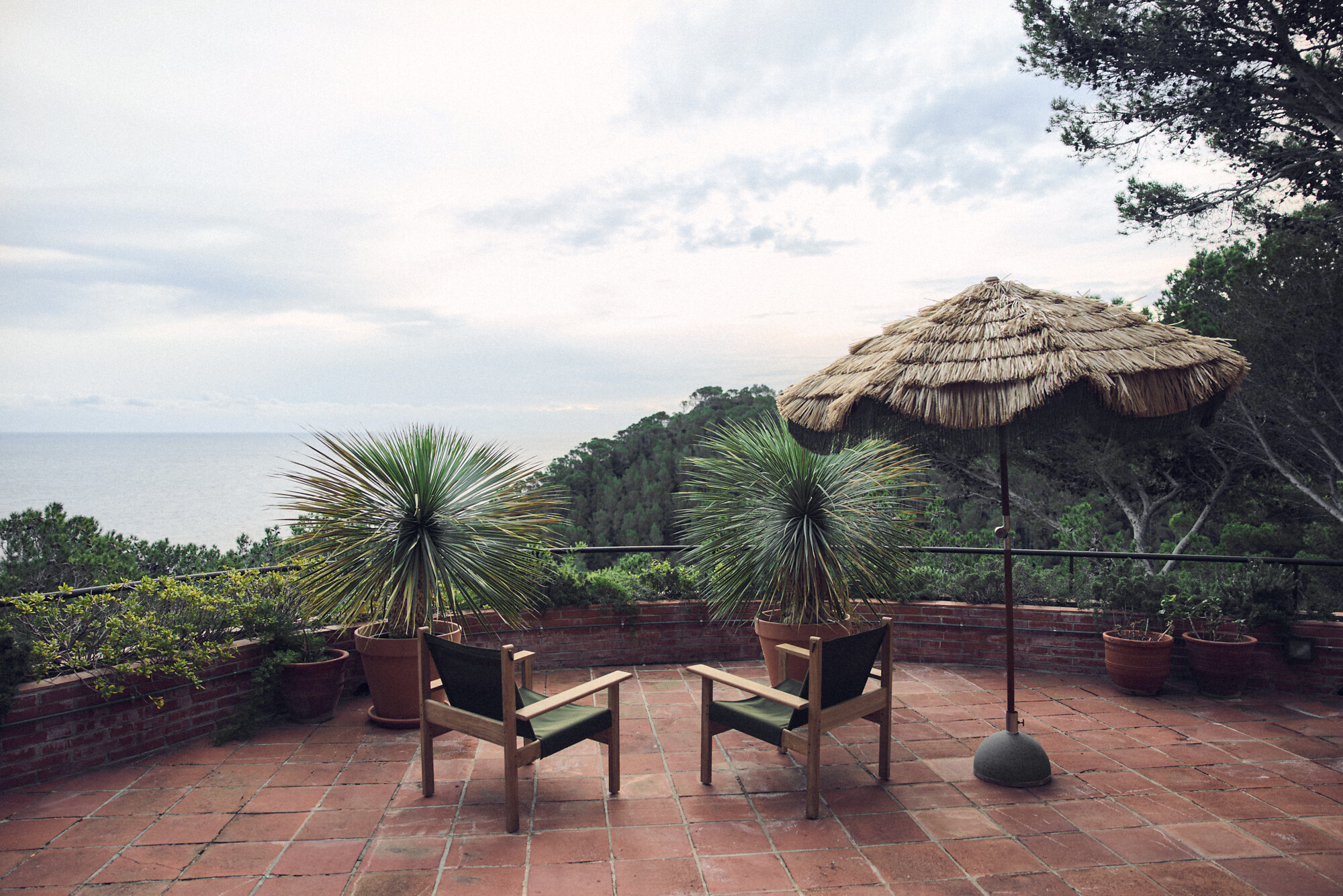 Zwei Outdoor-Stühle aus Holz mit Olivbespannung auf Terrasse mit Blick auf Küste  