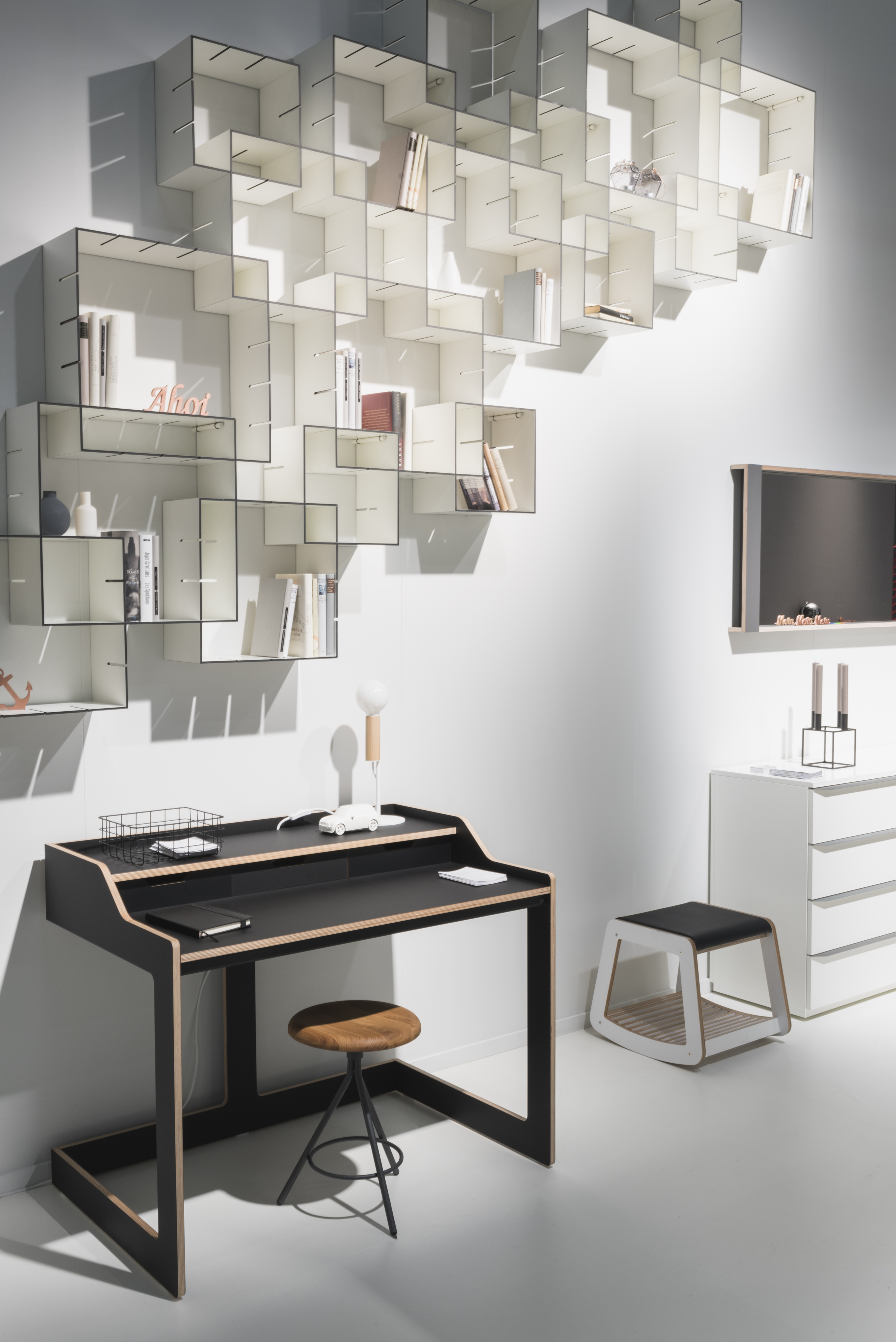 Schreibtisch mit schwarzer Oberfläche vor wandmontiertem Regal in Würfelstruktur