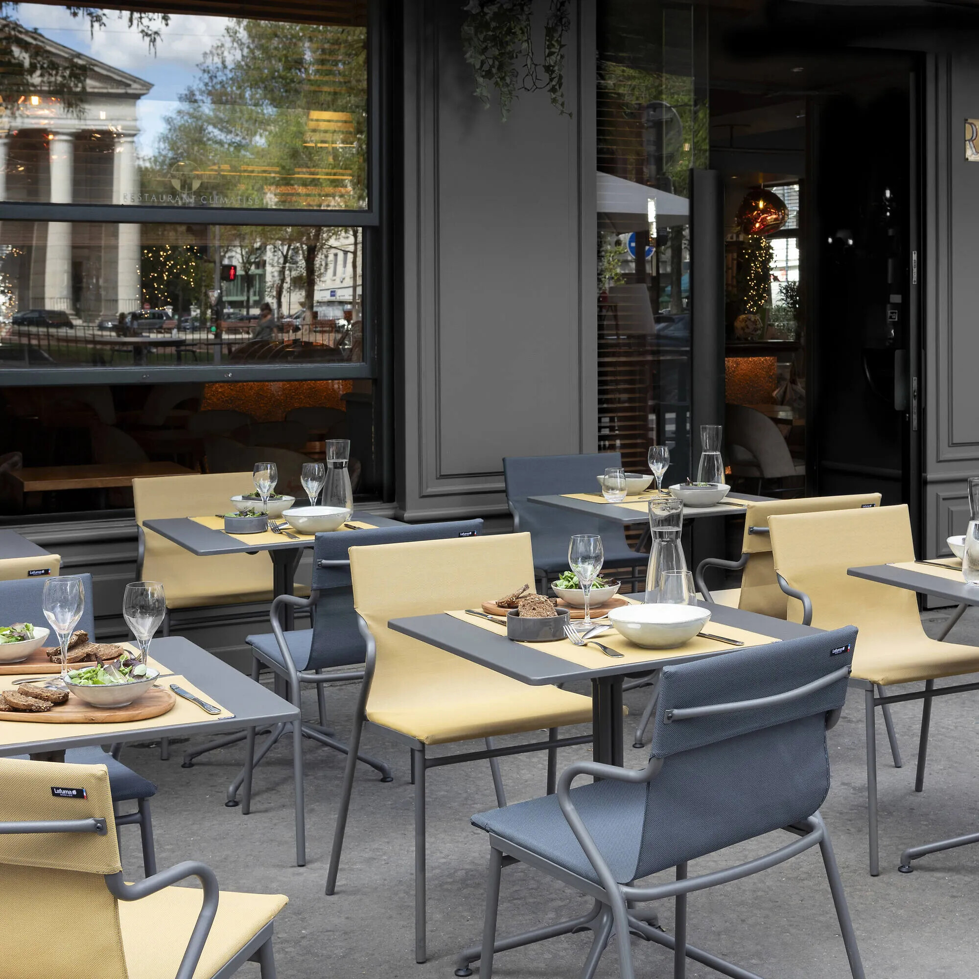 Outdoor-Bestuhlung mit gelben und blauen Sesseln und gedeckten Tischen vor Restaurant