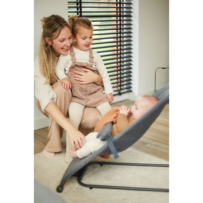Frau mit Kleinkind betrachtet lächelnd ein Baby in einer grauen Wippe von Childhome