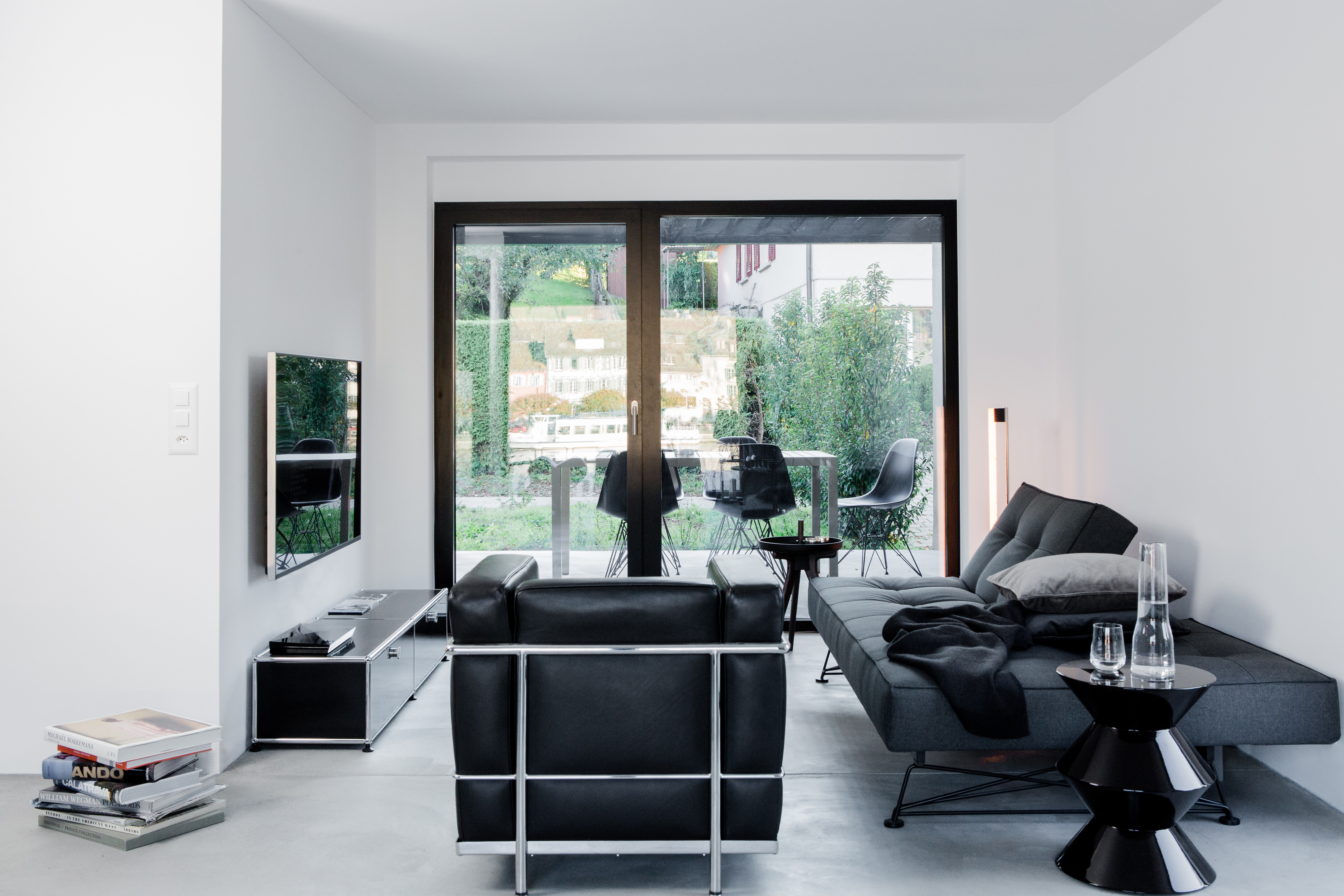 Die dunklen Töne des Wohnzimmers bieten den Kontrast zu dem lichtdurchfluteten Raum. Der Sessel LC 2 von Cassina sticht besonders heraus.