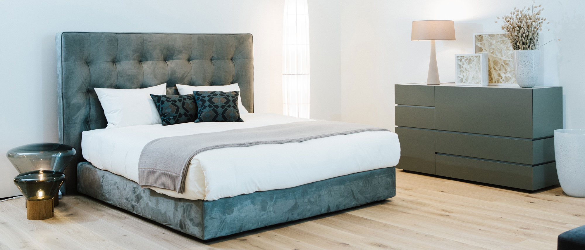 Gepolstertes Doppelbett mit hohem Kopfteil und grauer Kommode in modernem Schlafzimmer-Setting