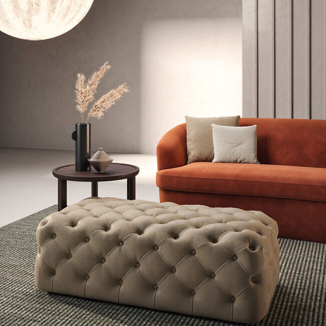 Gesteppter Pouf vor rostrotem Sofa mit beigen Kissen und Beistelltisch  