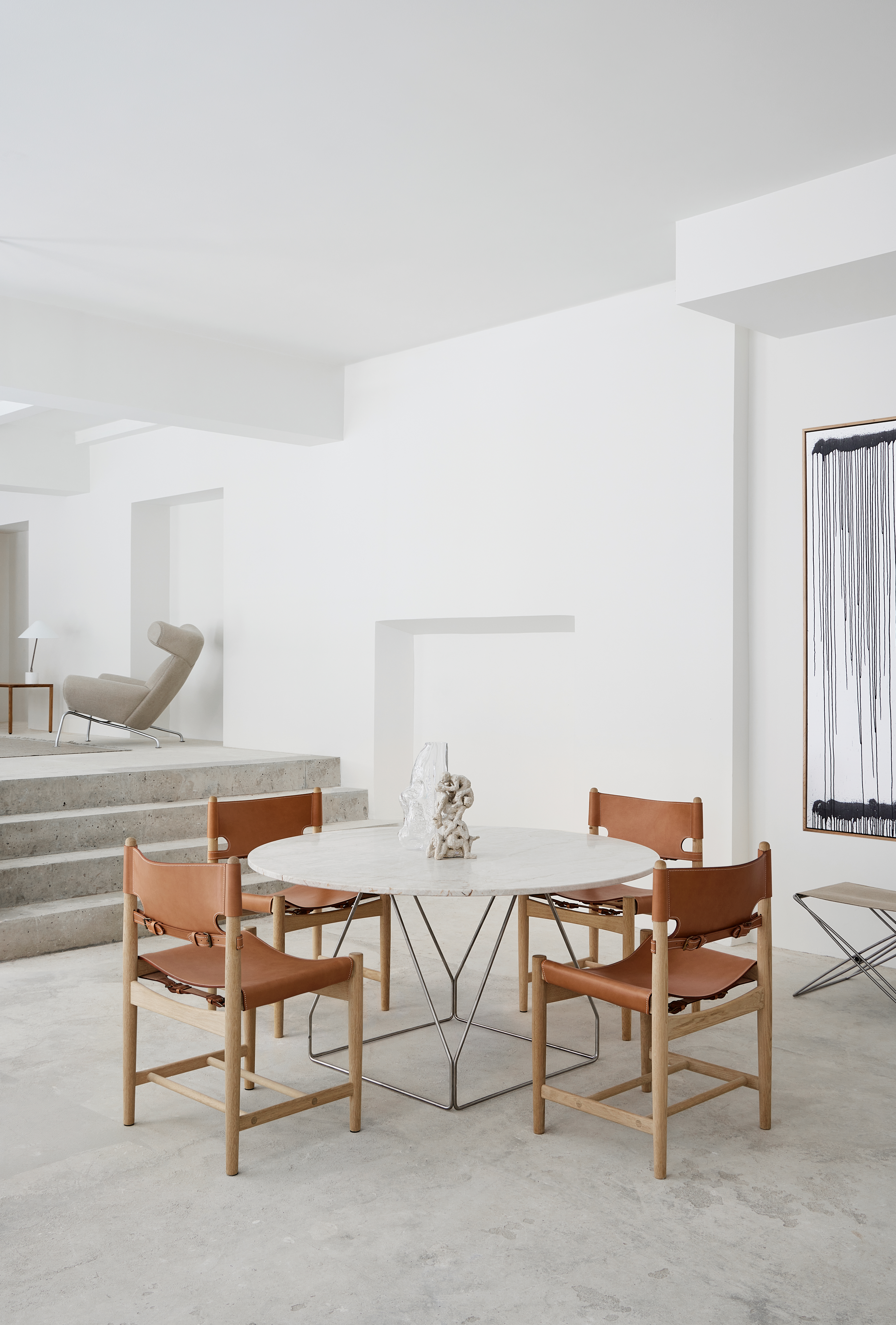 Vier Holzstühle mit Ledersitz an rundem Tisch vor heller Wand in offenem Raum