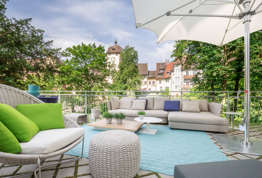 Outdoor-Ausstellungsfläche von Seipp Wohnen in Waldshut mit Lounge-Möbeln, Sonnenschirm und Blick auf die Altstadt.