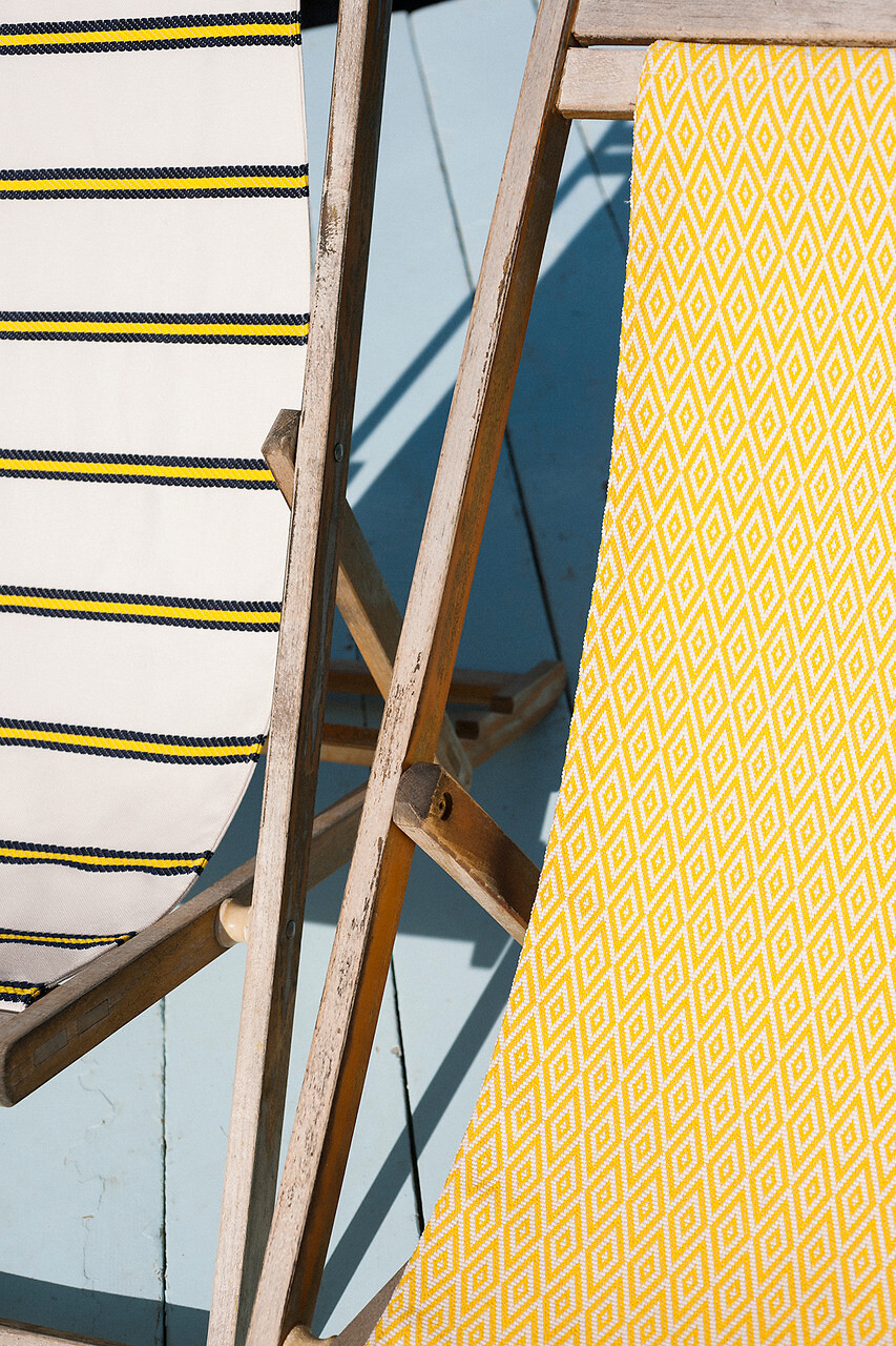 Zwei Holzliegestühle mit unterschiedlich gemusterten Dedar-Stoffen auf hellem Holzdeck