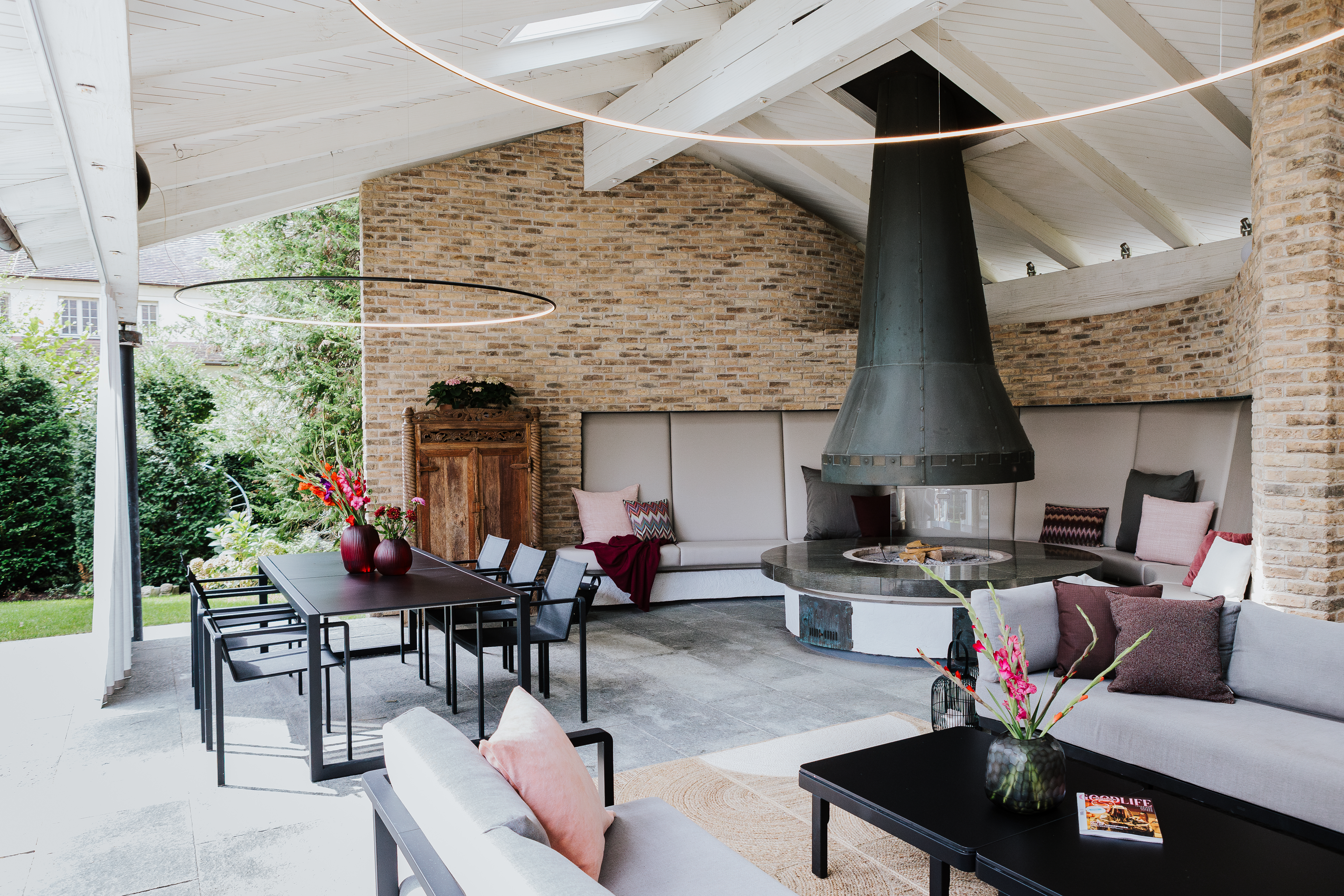 Überdachte Veranda mit gemauertem Kamin, großzügiger Sitzbank und Esstisch im Grünen.  