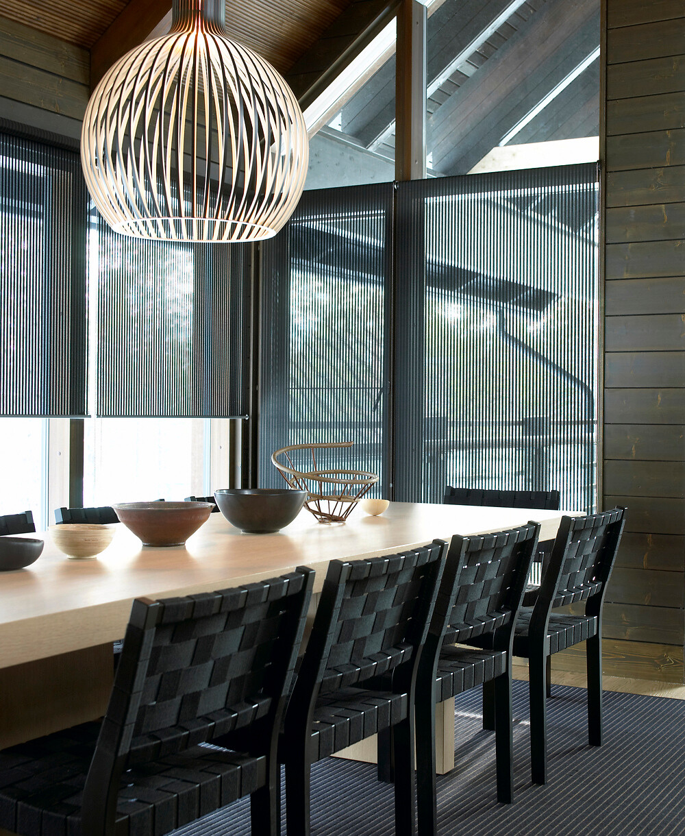 Großer Esstisch mit schwarzen Geflechtstühlen vor raumhohen Lamellenstores