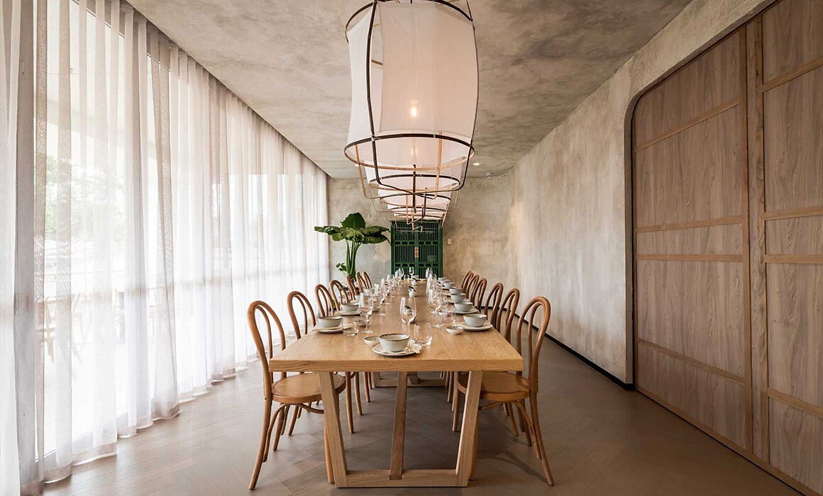 Langer Esstisch aus Holz mit gedeckter Tafel unter großformatigen Hängeleuchten