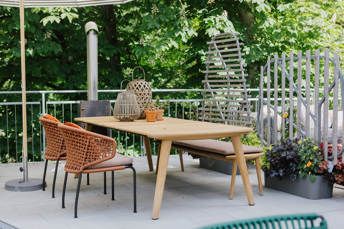 Outdoor-Essplatz mit geflochtenen Armlehnenstühlen und Holzbank an einem Tisch aus Teakholz auf der Terrasse der Gartenmöbelausstellung in Waldshut bei Seipp Wohnen