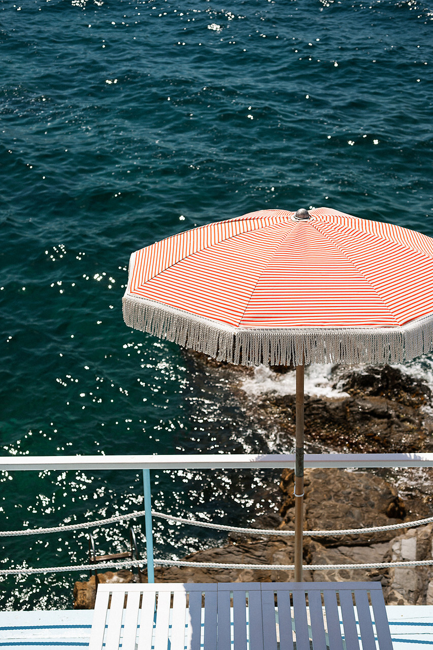 Gestreifter Sonnenschirm mit Fransenbesatz von Dedar an einer Küstenpromenade am Wasser