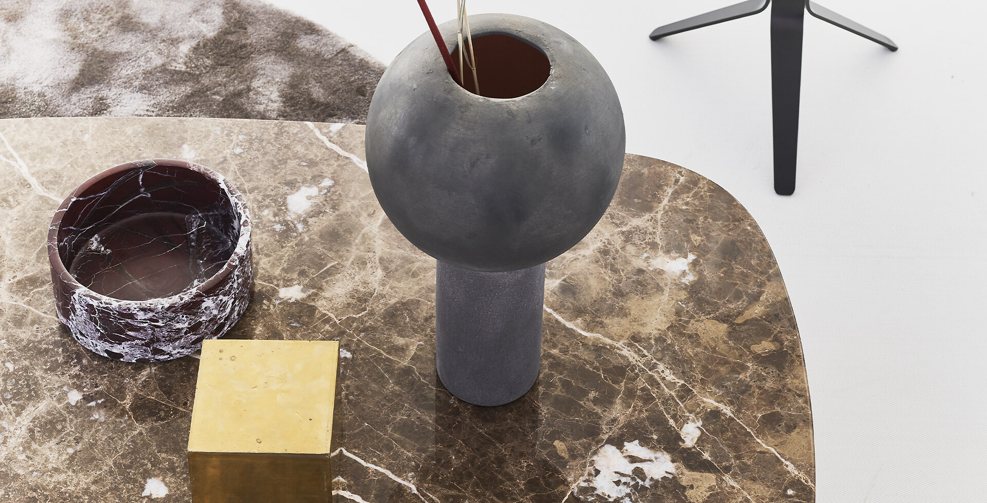 Runde graue Vase mit Stäben, auf Marmorplatte mit goldfarbenem Akzent auf Tisch platziert  