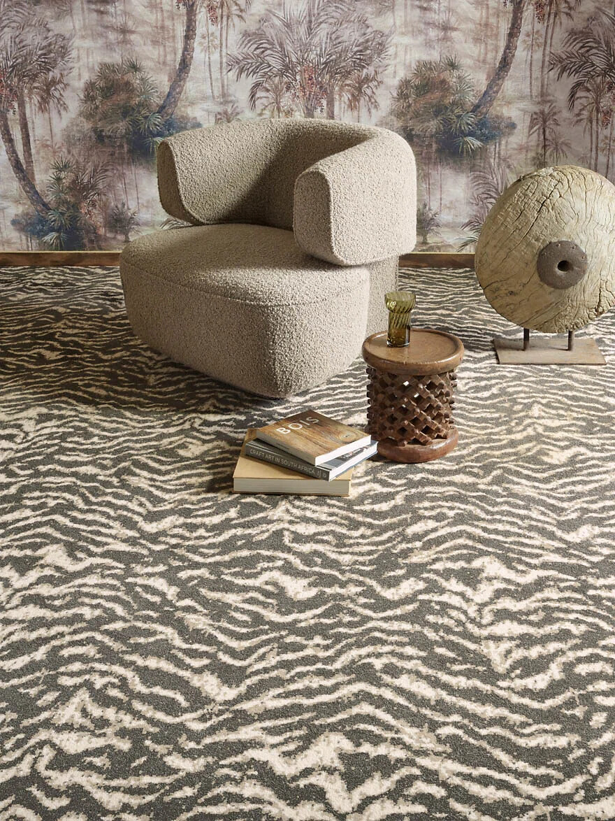 Teppich mit abstraktem Zebramuster in Beige und Dunkelgrau, Sessel im Vordergrund  