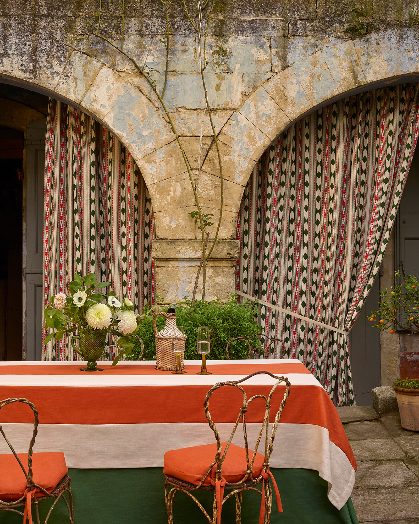 Gemusterte Vorhänge vor Sandsteinbogen mit gedecktem Esstisch im Freien  