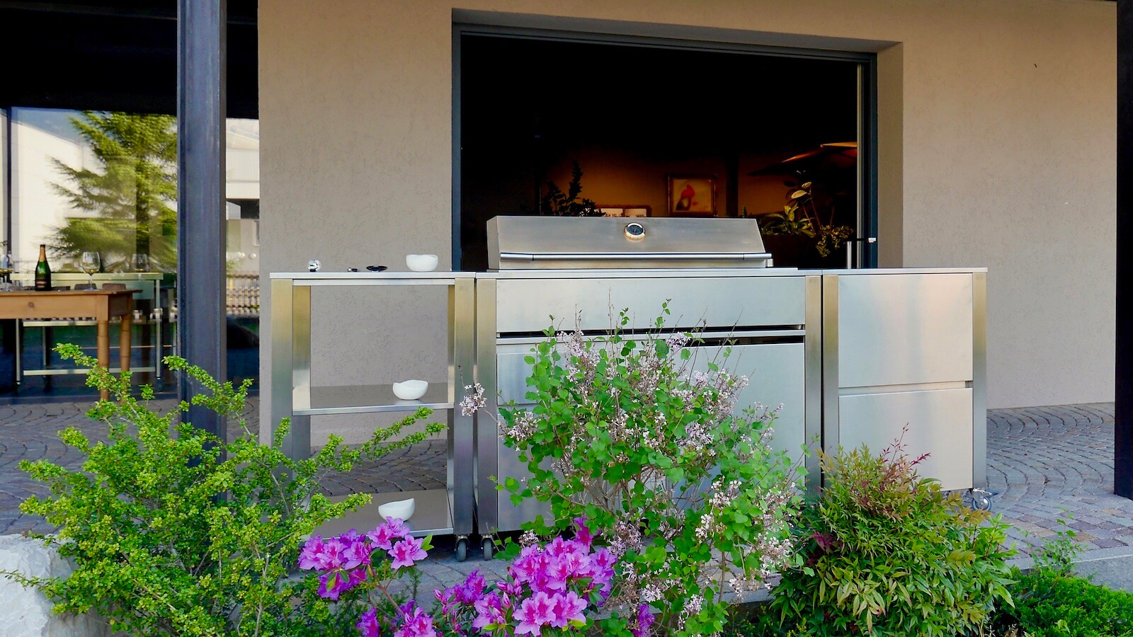 Modulare Außenküche von JOKODOMUS mit Grillmodul und Seitenmöbeln vor Hausfassade  