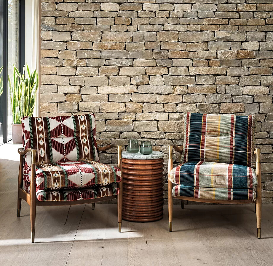 Zwei Sessel mit gemusterten Stoffbezügen vor Steinwand mit rundem Beistelltisch