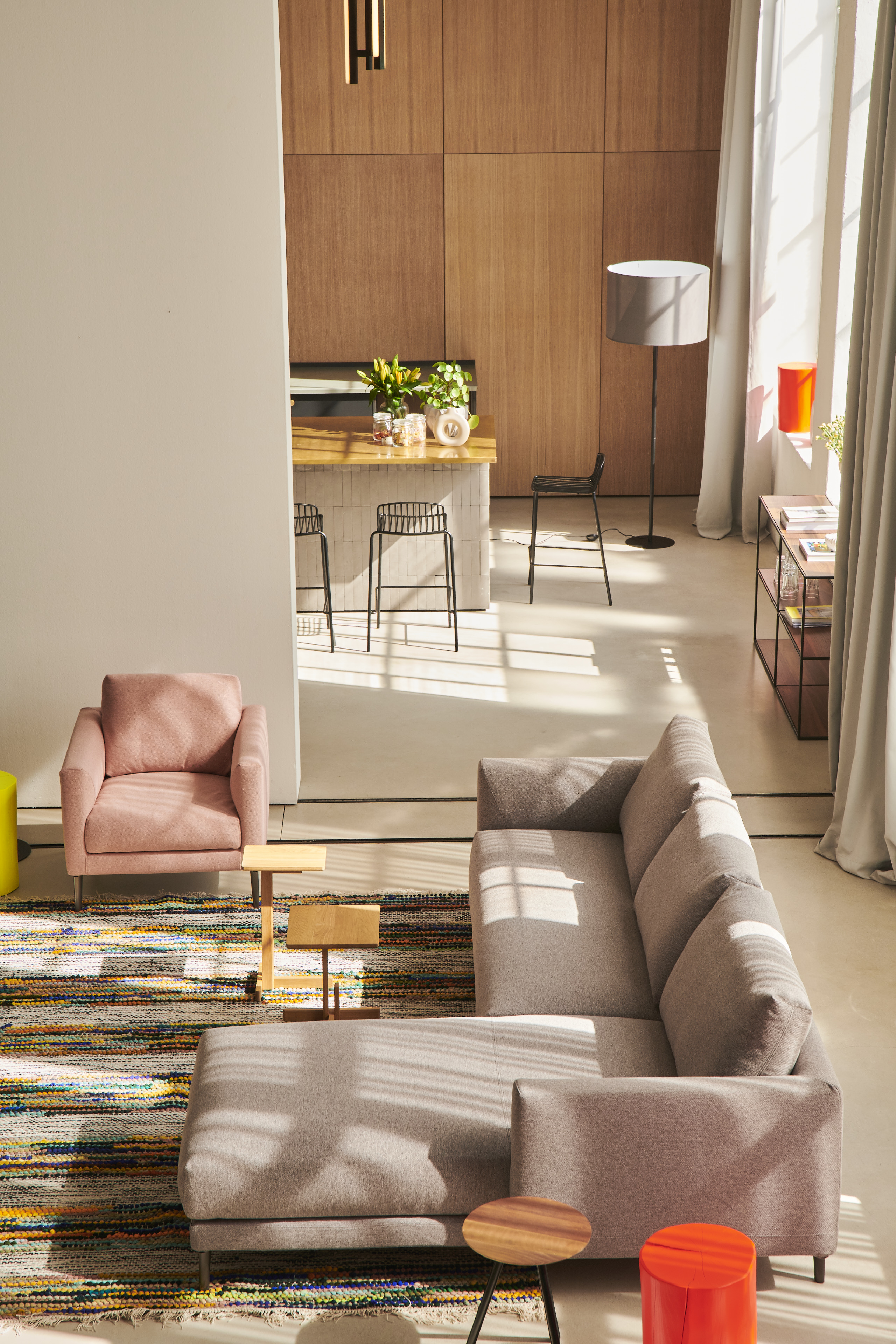 Wohnzimmer mit Ecksofa in Grauton, roséfarbenem Sessel und Teppich mit Streifenmuster