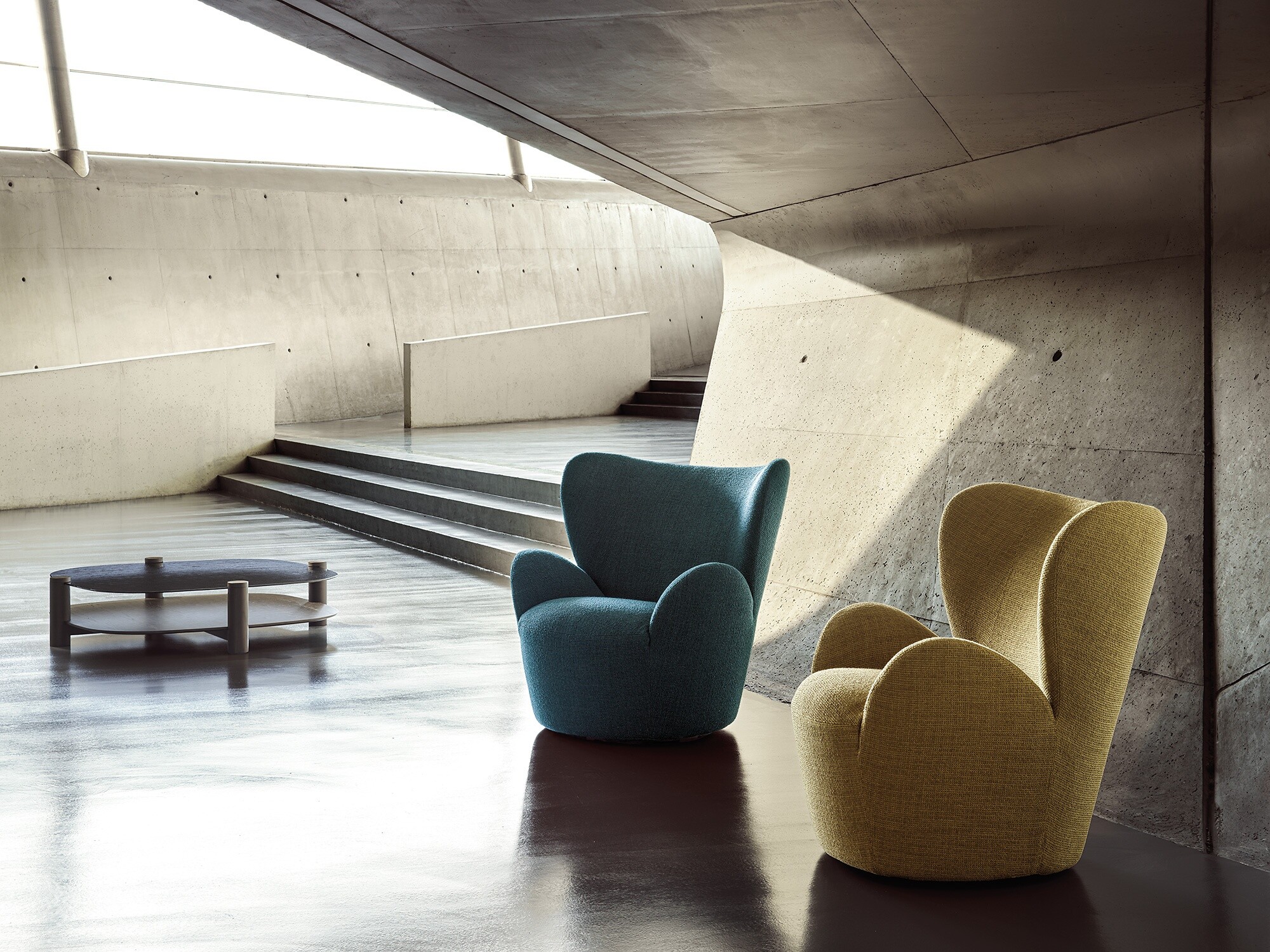 Zwei Polstersessel in Gelb und Blau in architektonisch markantem, lichtdurchflutetem Raum