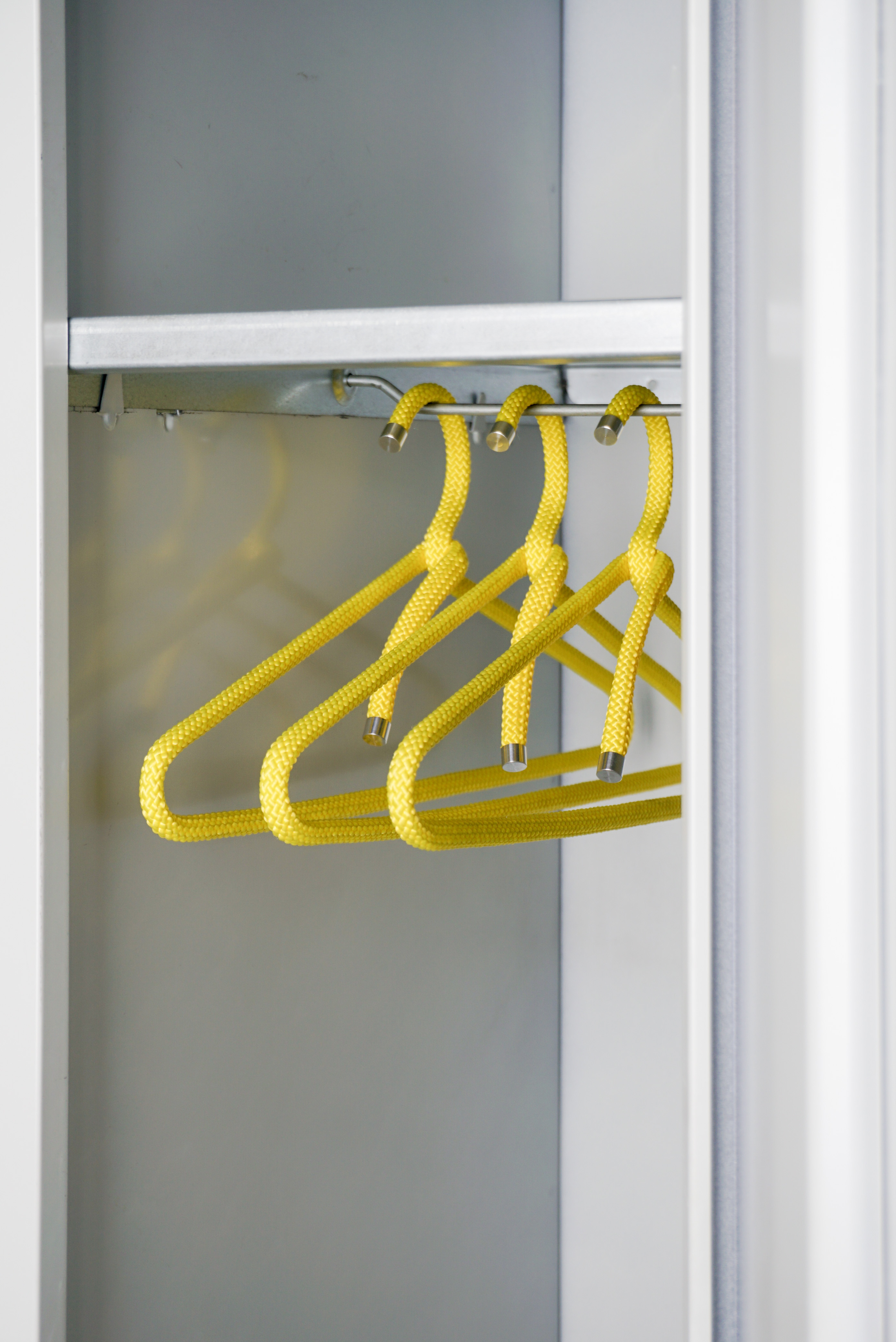 Mehrere gelbe Kleiderbügel aus Seilmaterial hängen geordnet in einem Schrank  