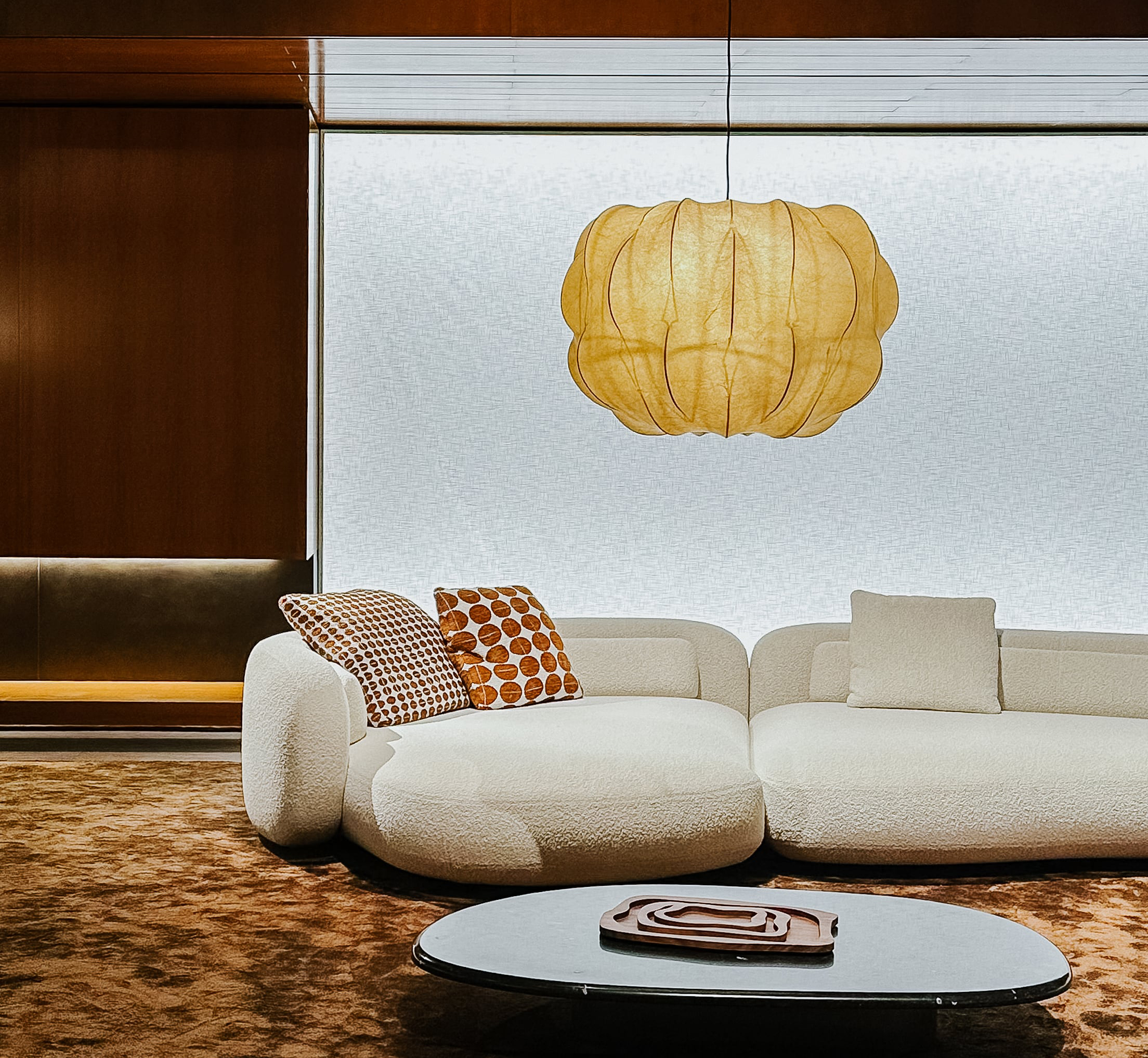 Wohnsituation mit Sofa in hellem Bouclé-Stoff, kombiniert mit naturfarbenem Teppich, grafischen Kissen und einer organischen Pendelleuchte. Der Raum wirkt ruhig, weich und stilvoll.