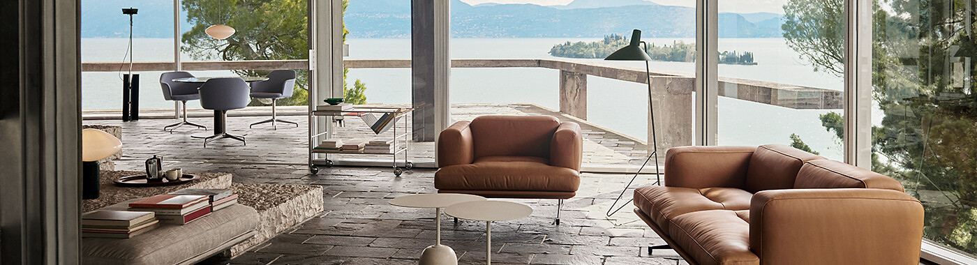 Wohnbereich mit cognacfarbenem Sofa, Glastisch und Ausblick auf See durch Fensterfront